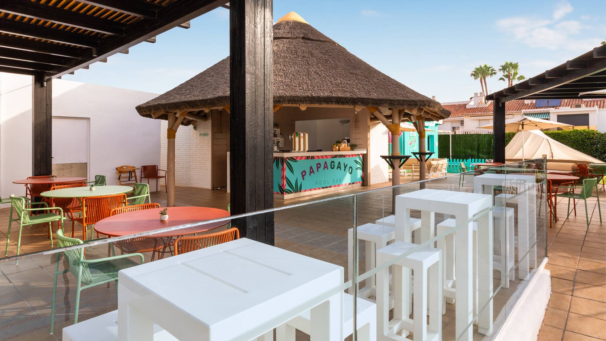 Terraza del Papagayo Pool Bar con quiosco de tejado de paja y mesas coloridas.