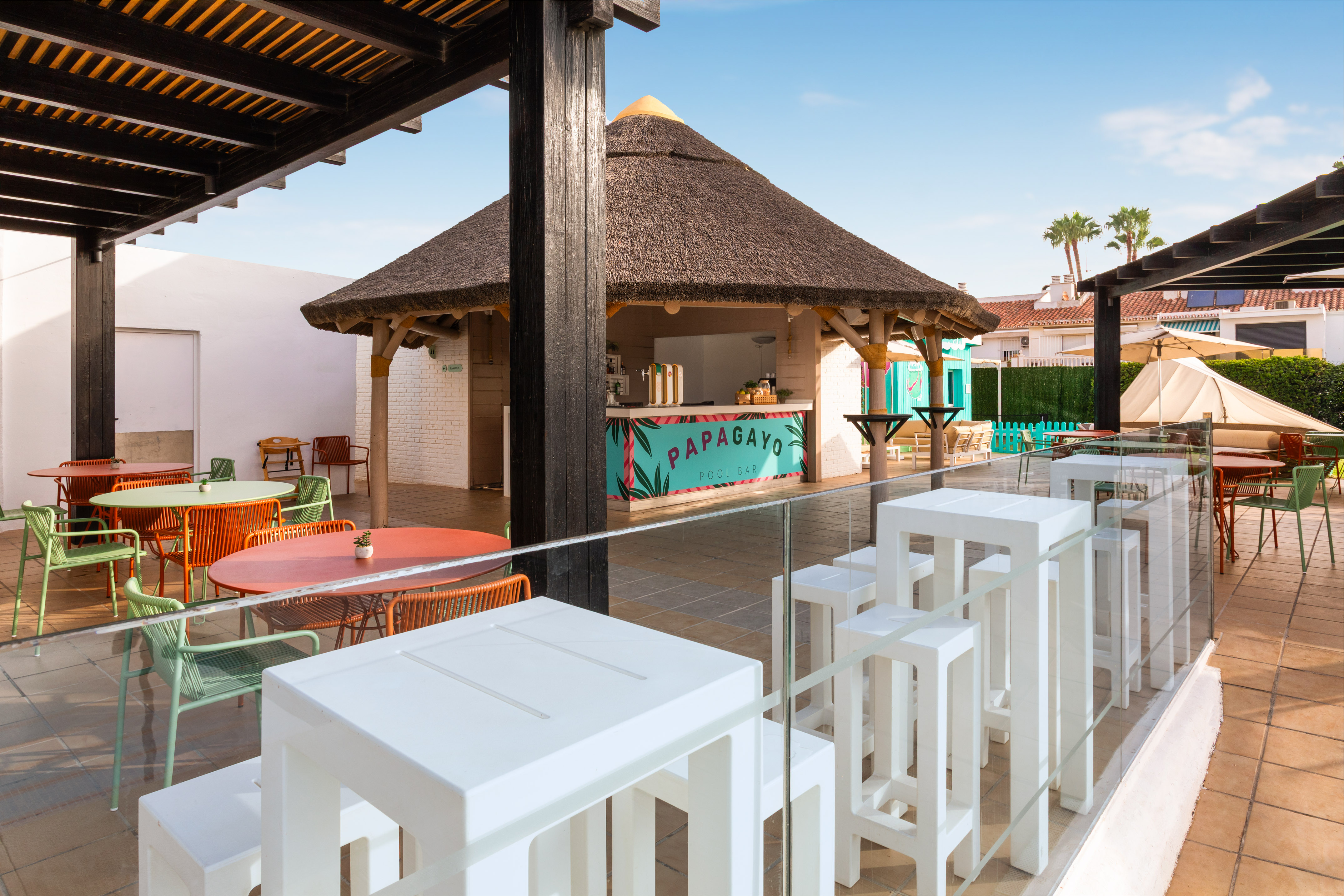 Terraza del Papagayo Pool Bar con quiosco de tejado de paja y mesas coloridas.