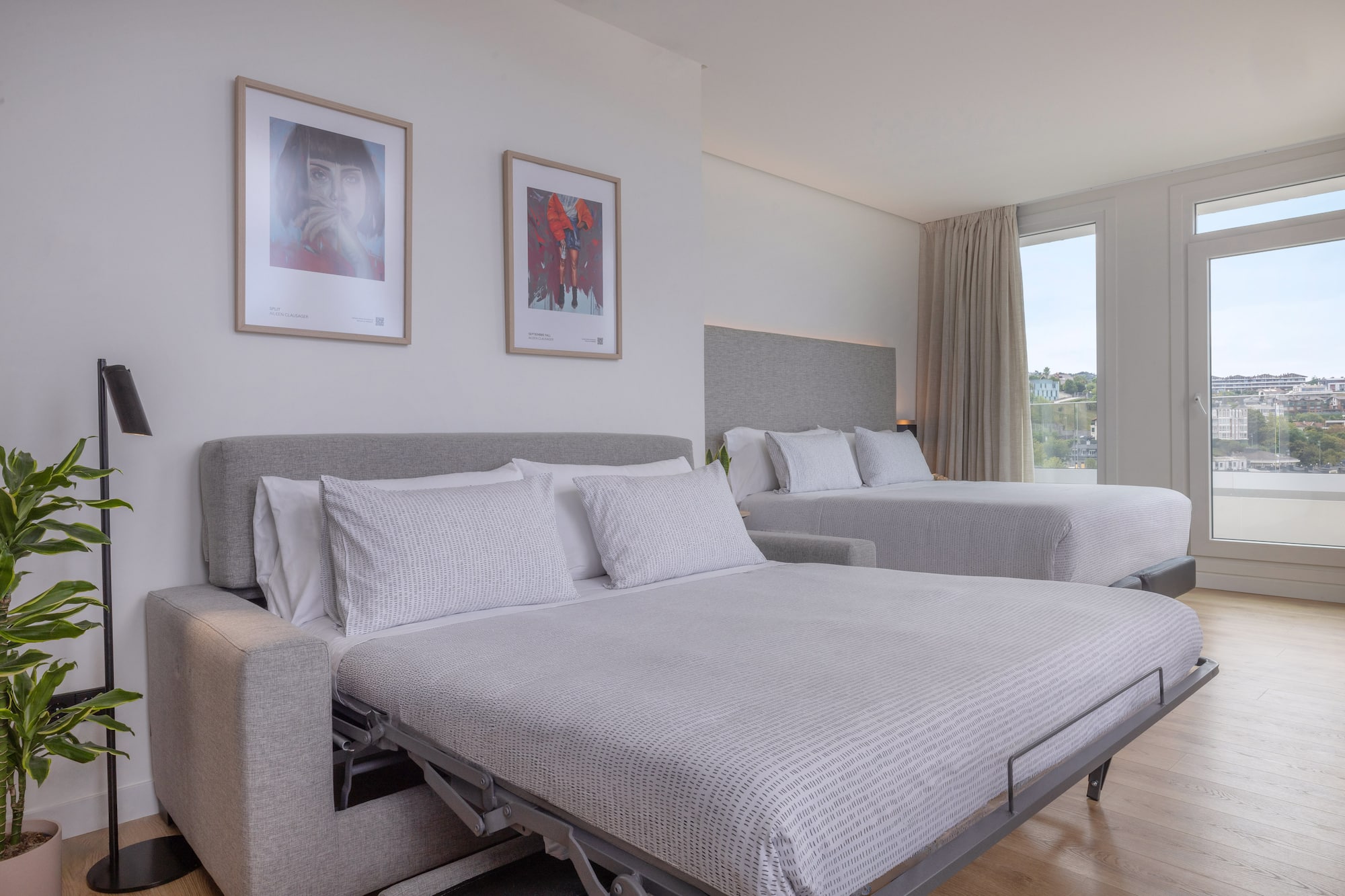 Habitación de hotel moderna con sofá cama, cama doble, ventanales y vistas.