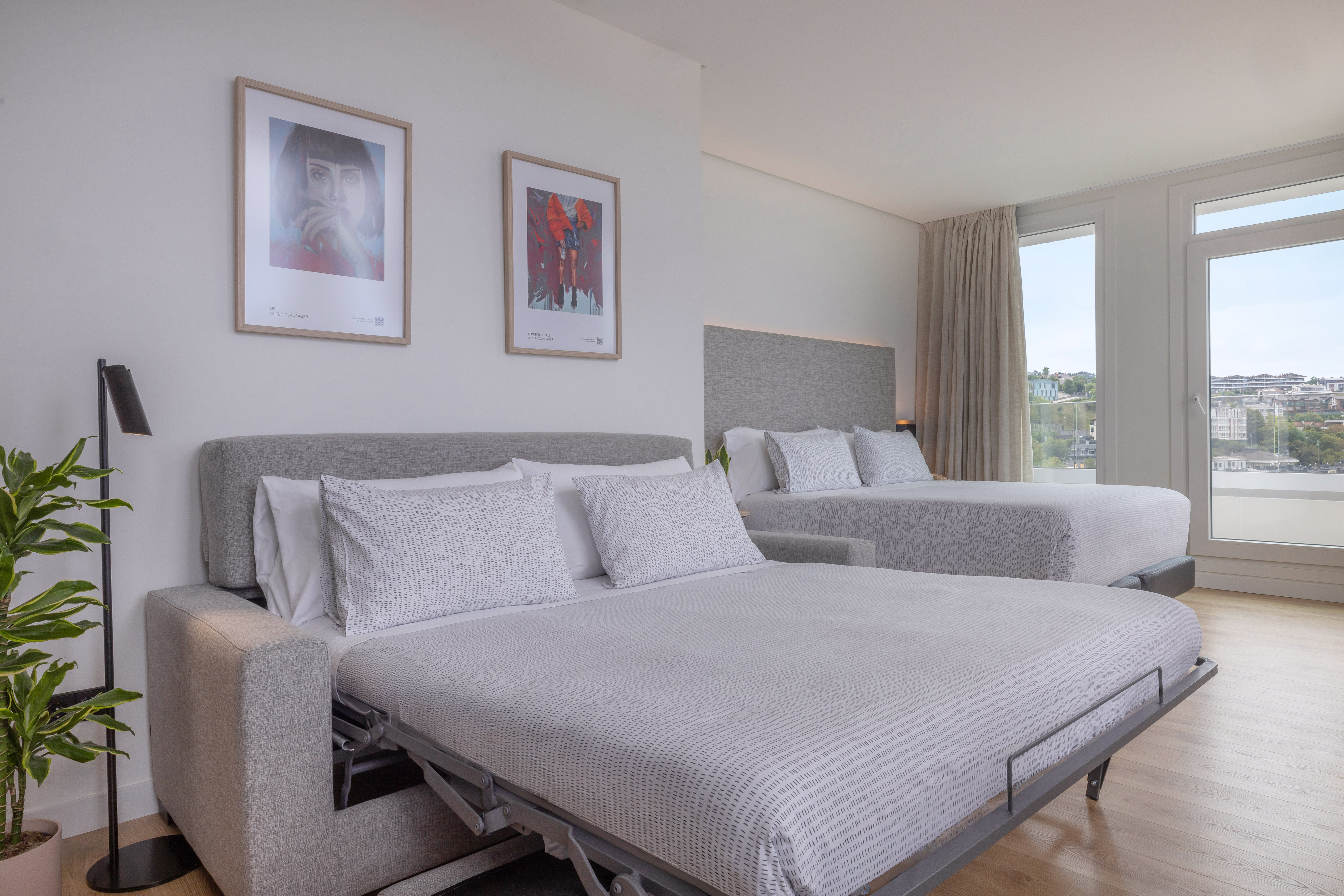 Habitación de hotel moderna con sofá cama, cama doble, ventanales y vistas.