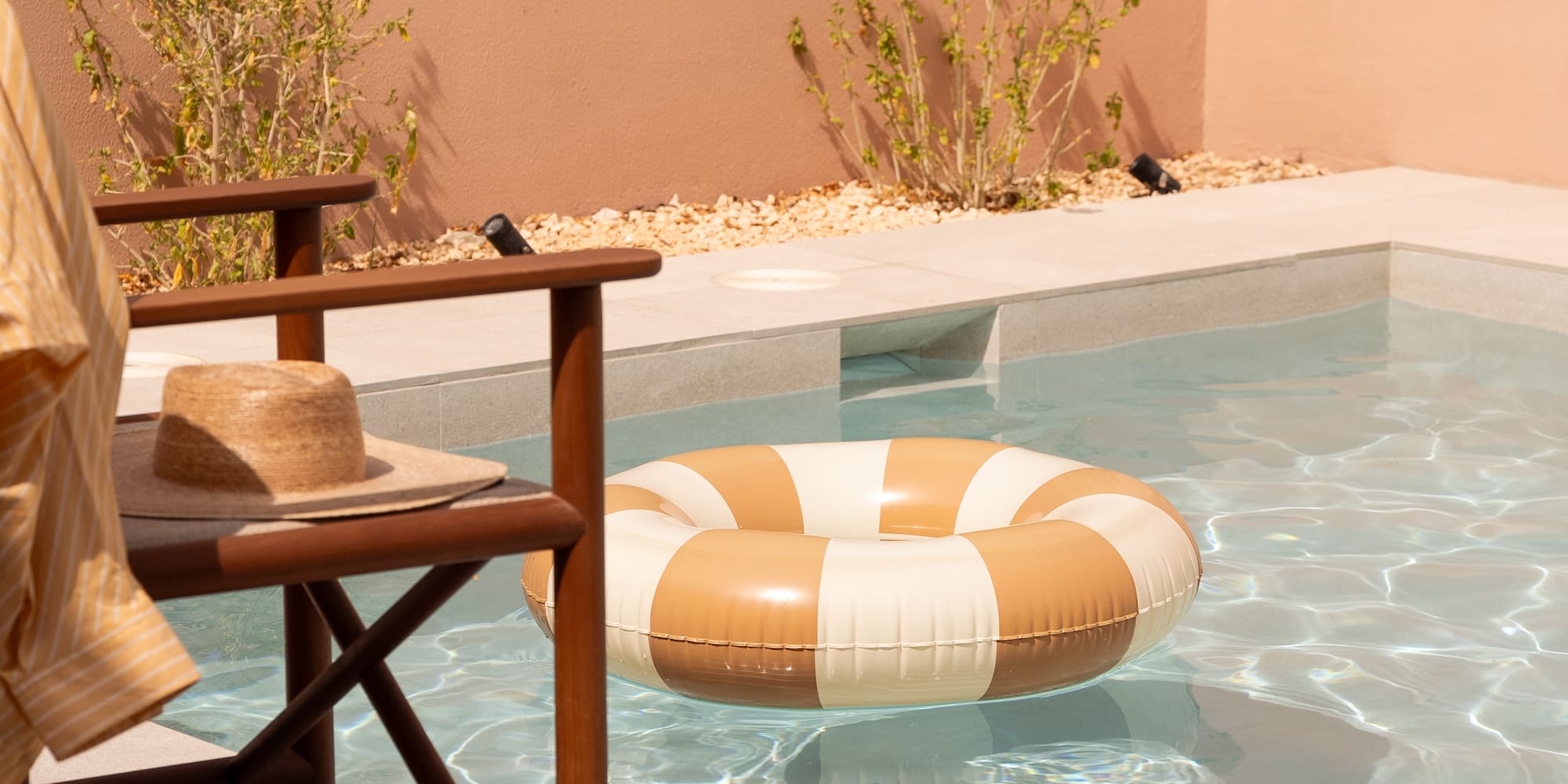 Private pool with striped float, straw hat on chair, and sandals.