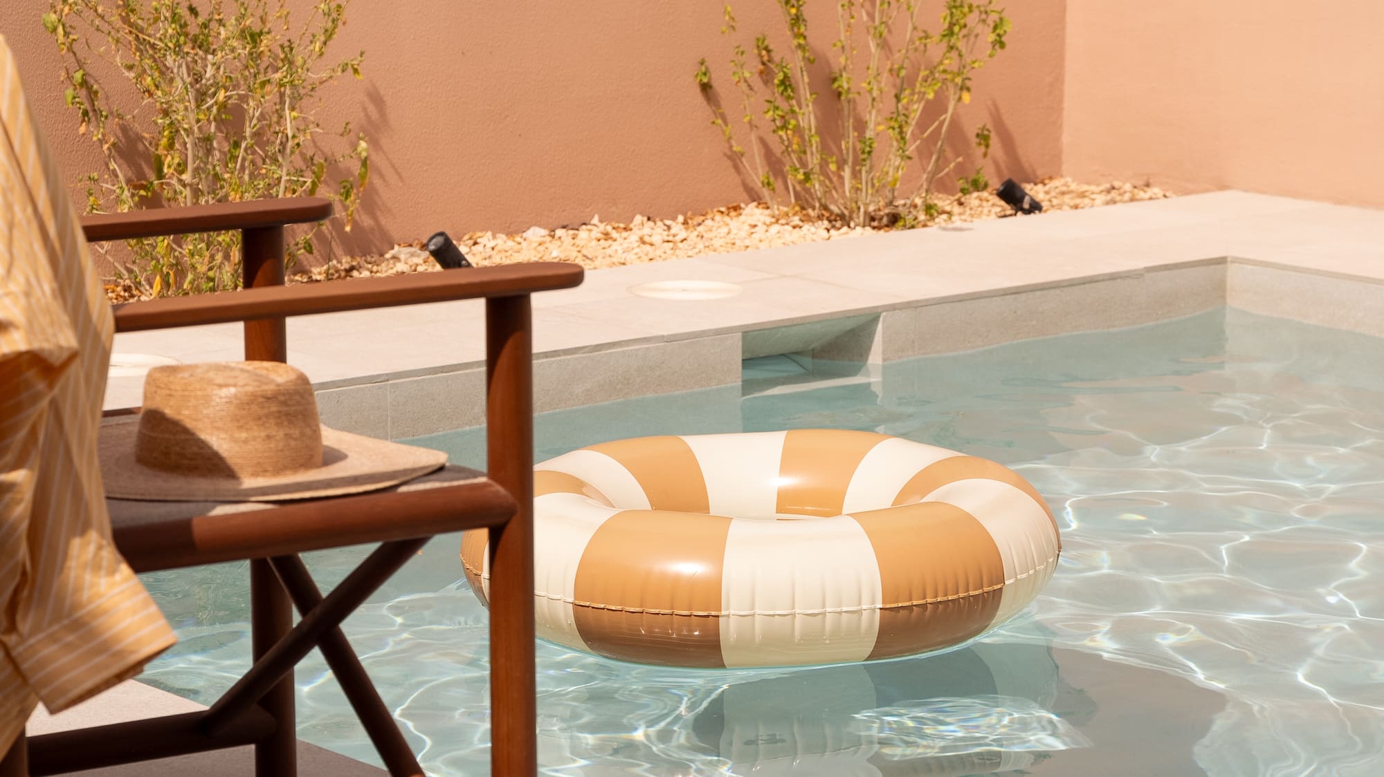 Private pool with striped float, straw hat on chair, and sandals.