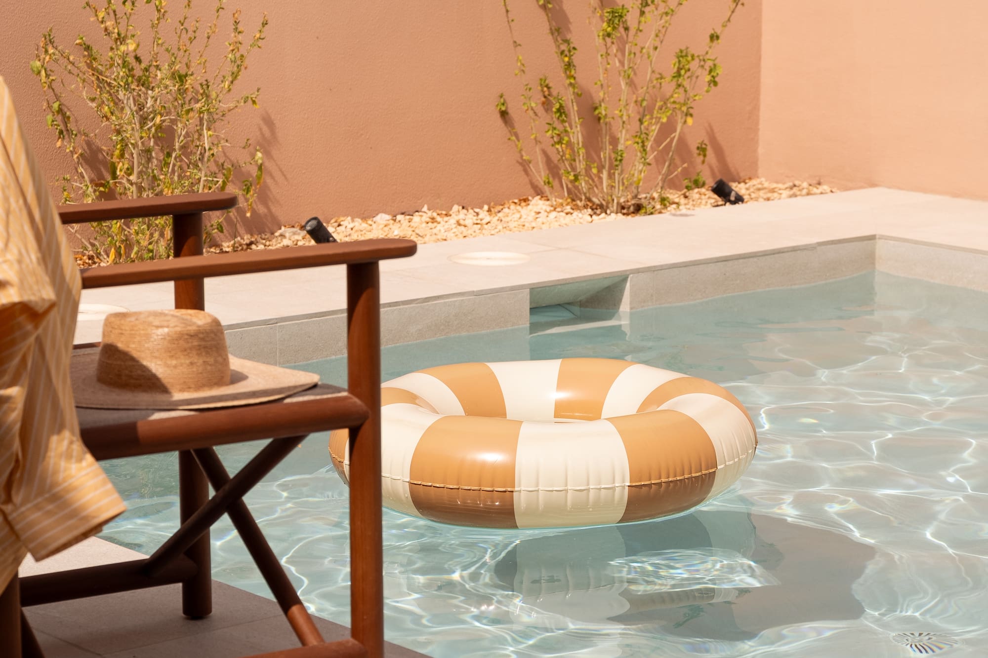Private pool with striped float, straw hat on chair, and sandals.