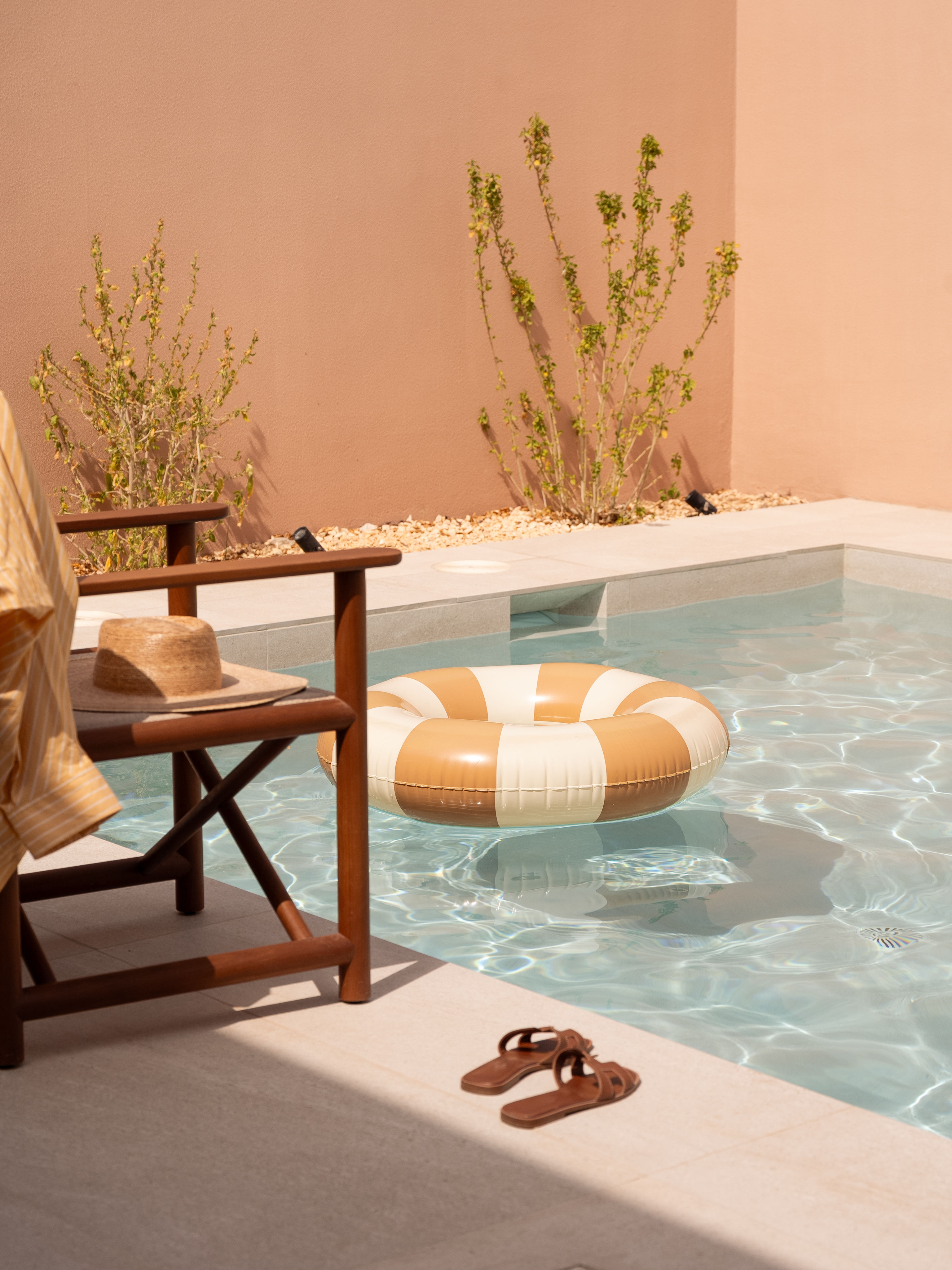 Private pool with striped float, straw hat on chair, and sandals.