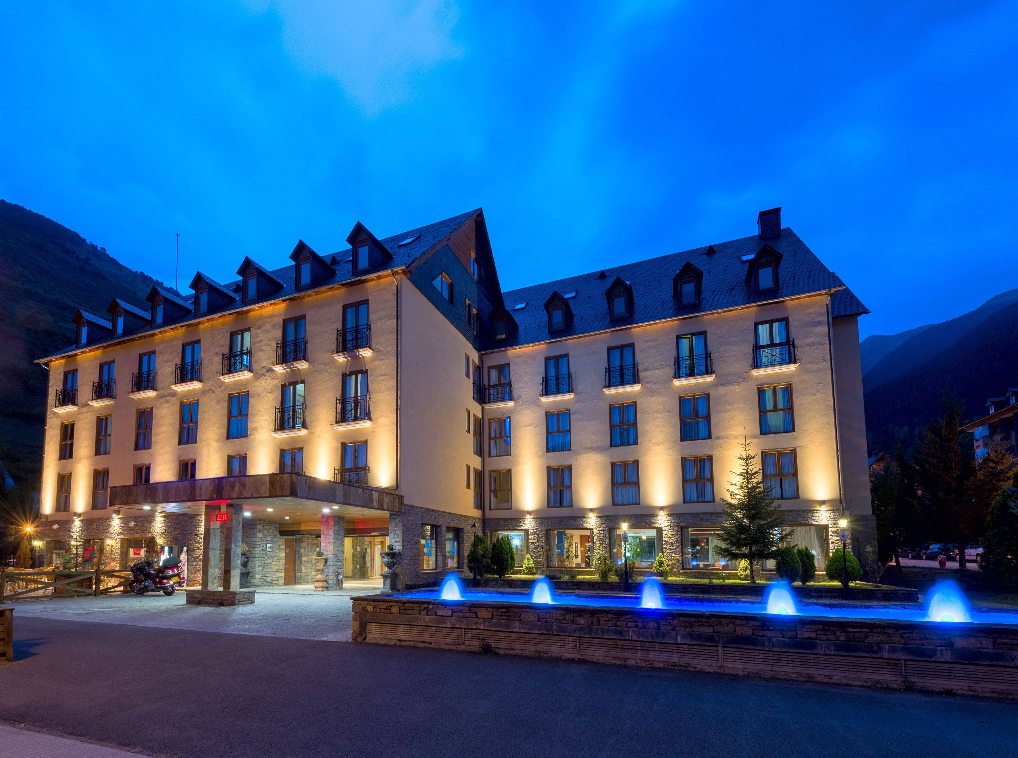 Illuminated mountain hotel exterior at night with blue fountains.