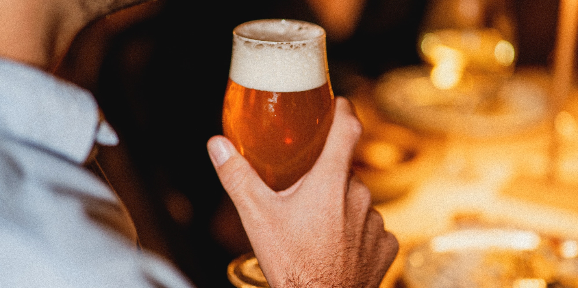 Smiling man holding amber beer in a warm, dimly lit bar.