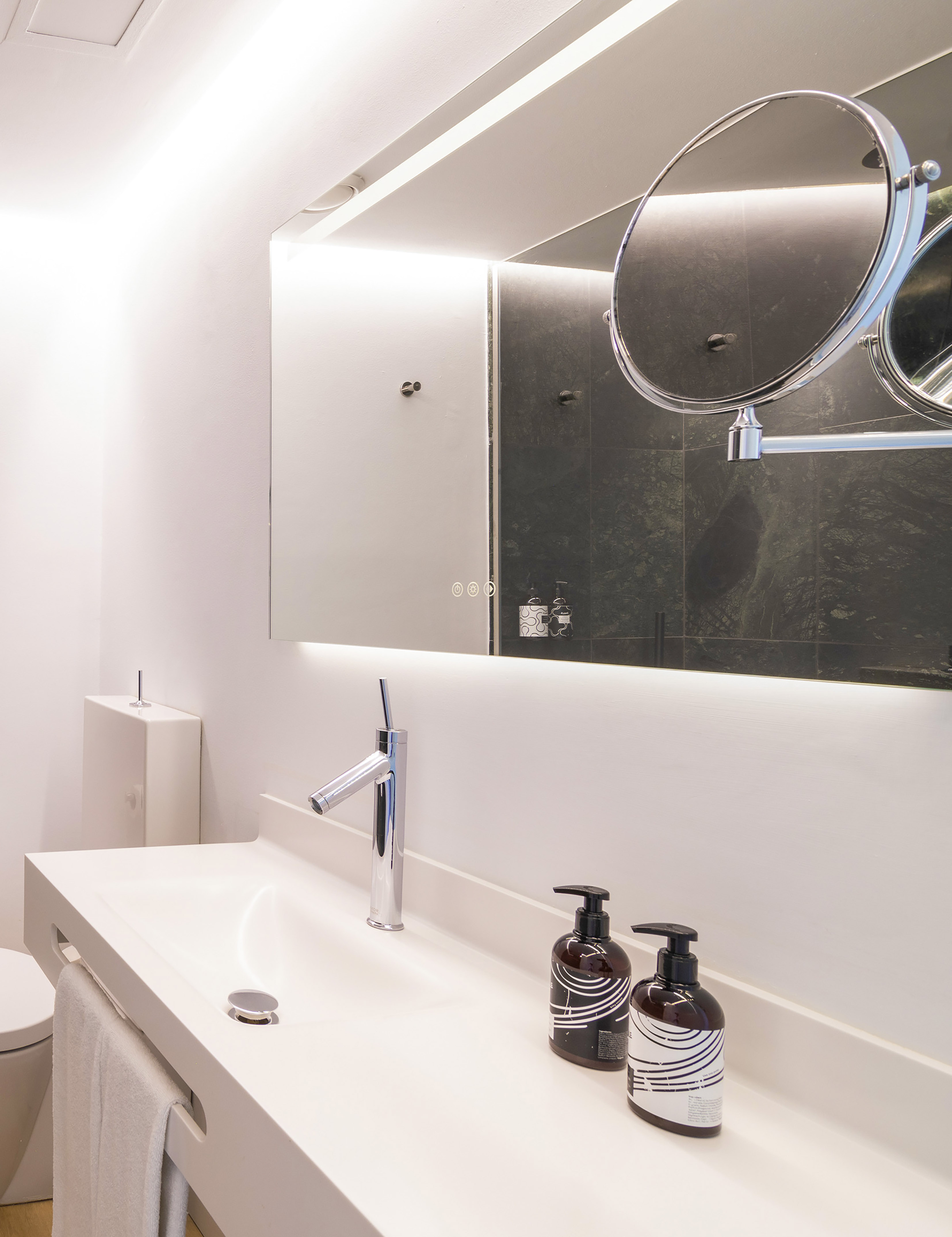 Modern white bathroom vanity, chrome faucet, and backlit mirror.