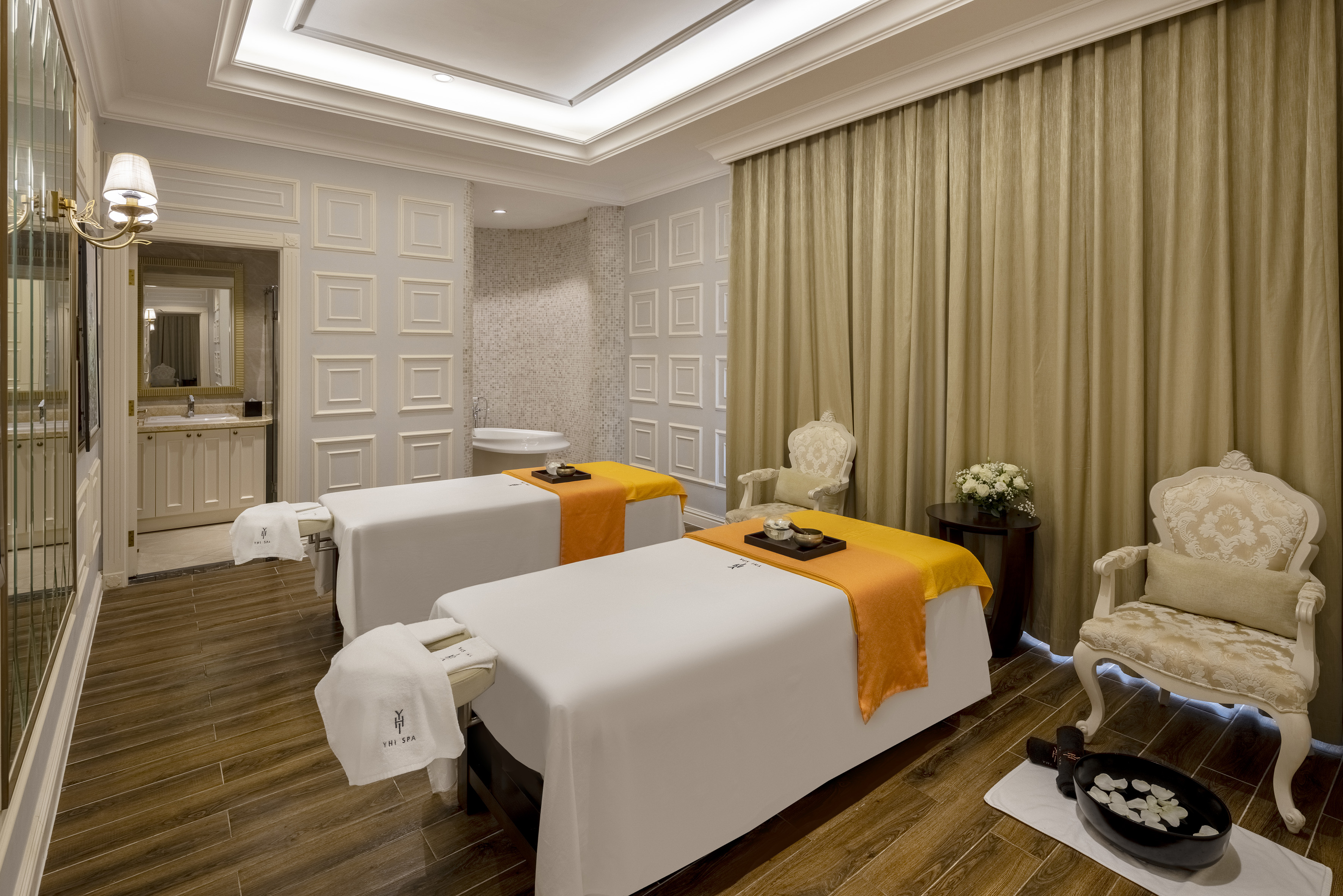 Luxury spa treatment room with two massage beds, elegant decor, and foot bath.