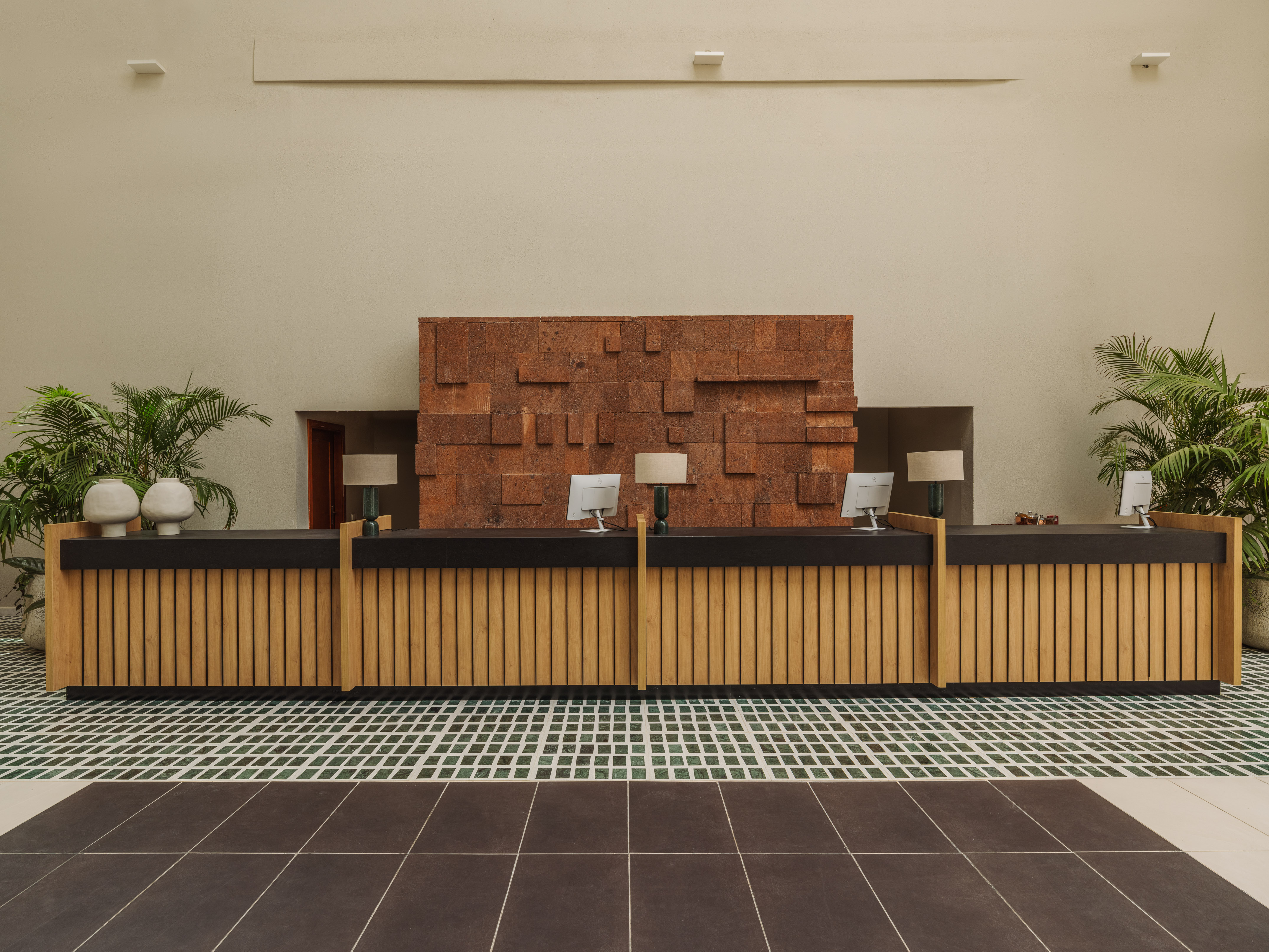 Modern hotel check-in desk with wooden slats, textured wall, and plants.