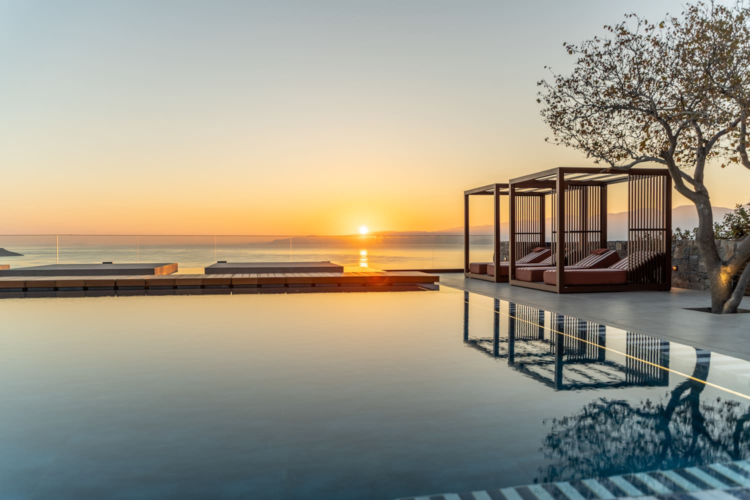 a pool with a gazebo and a tree and a sunset