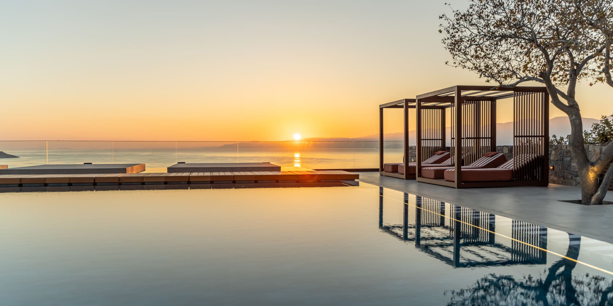 a pool with a gazebo and a tree and a sunset