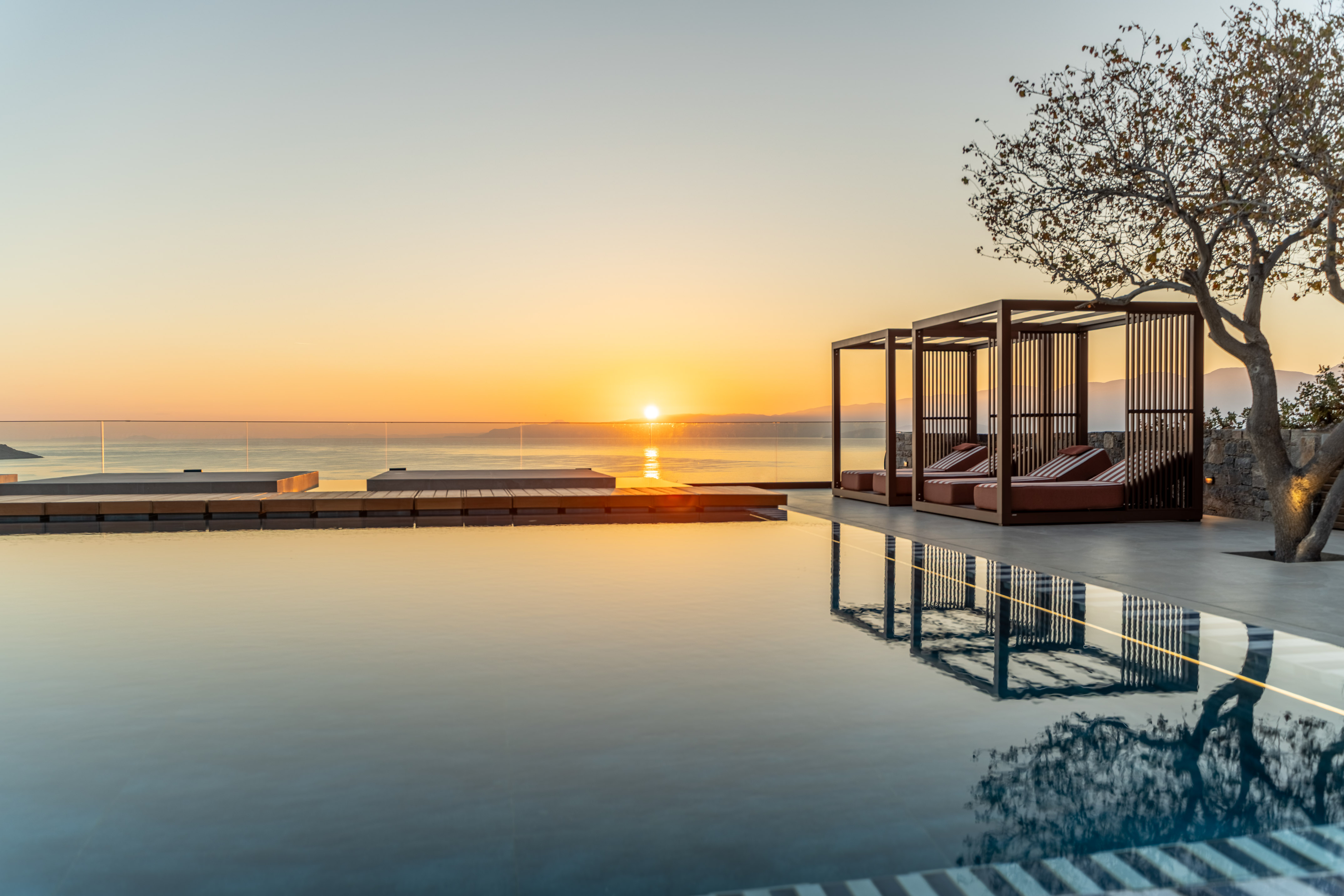 a pool with a gazebo and a tree and a sunset