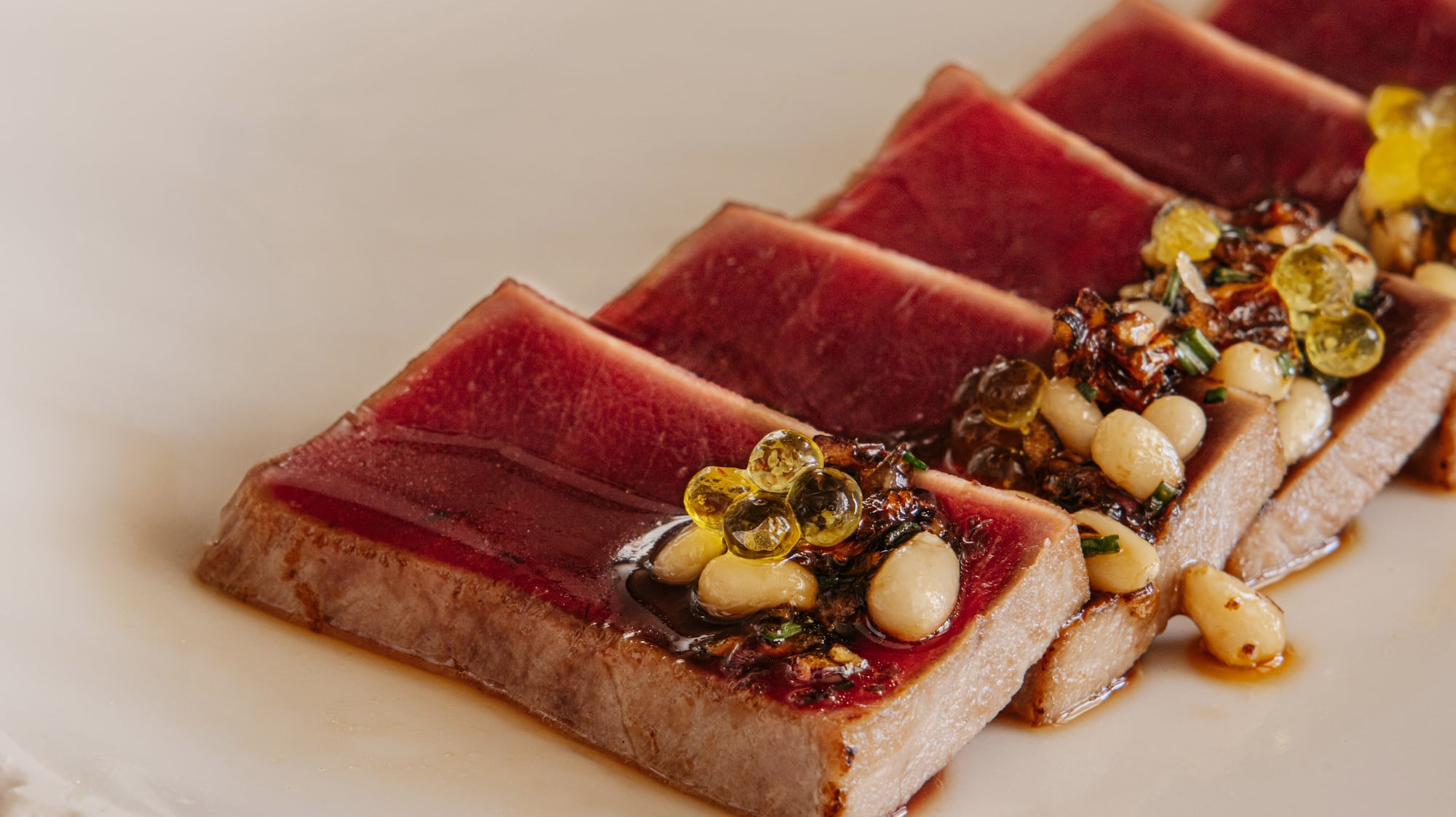 Seared tuna tataki with pine nuts, golden spheres, and savory sauce.