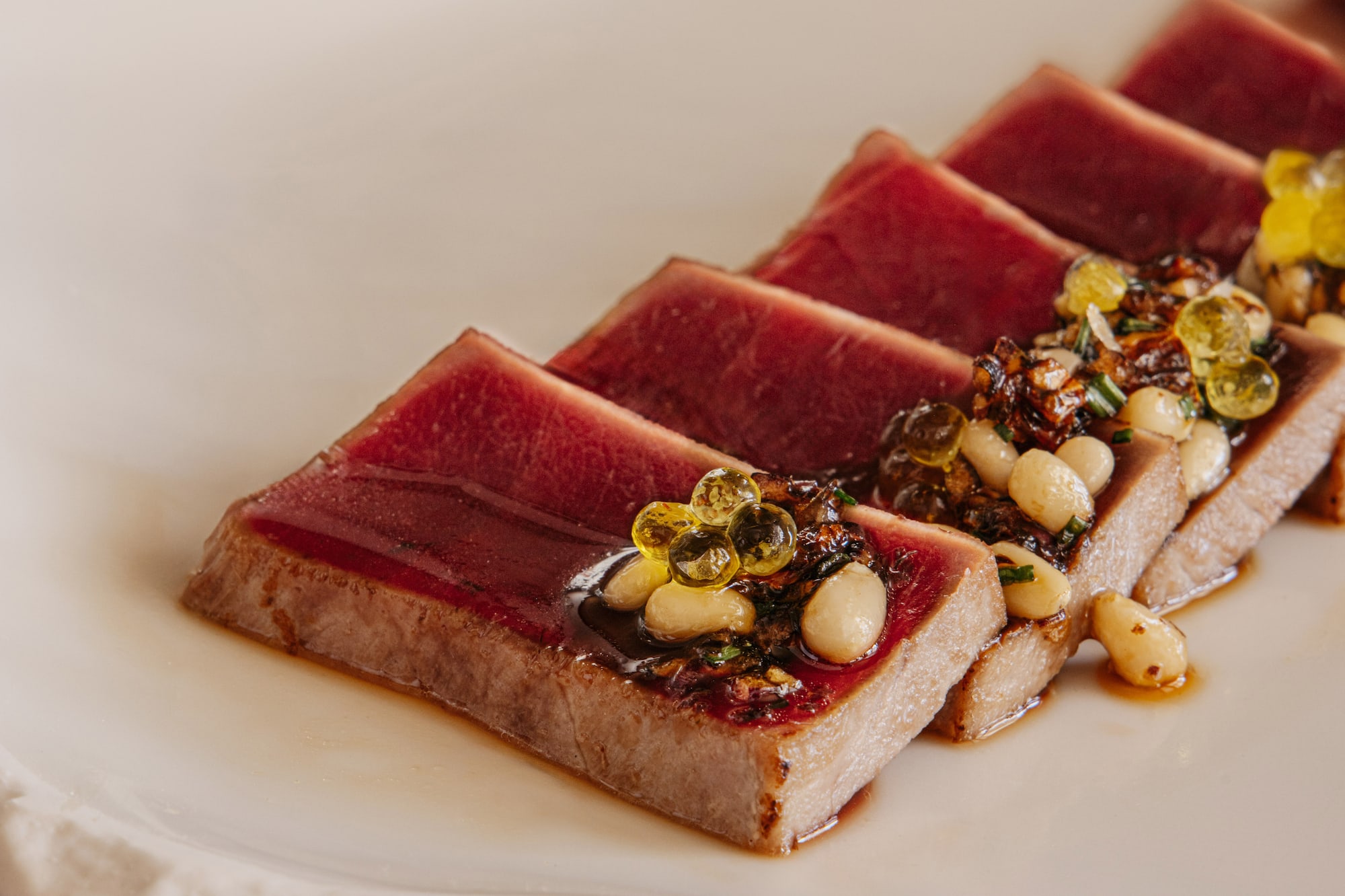 Seared tuna tataki with pine nuts, golden spheres, and savory sauce.