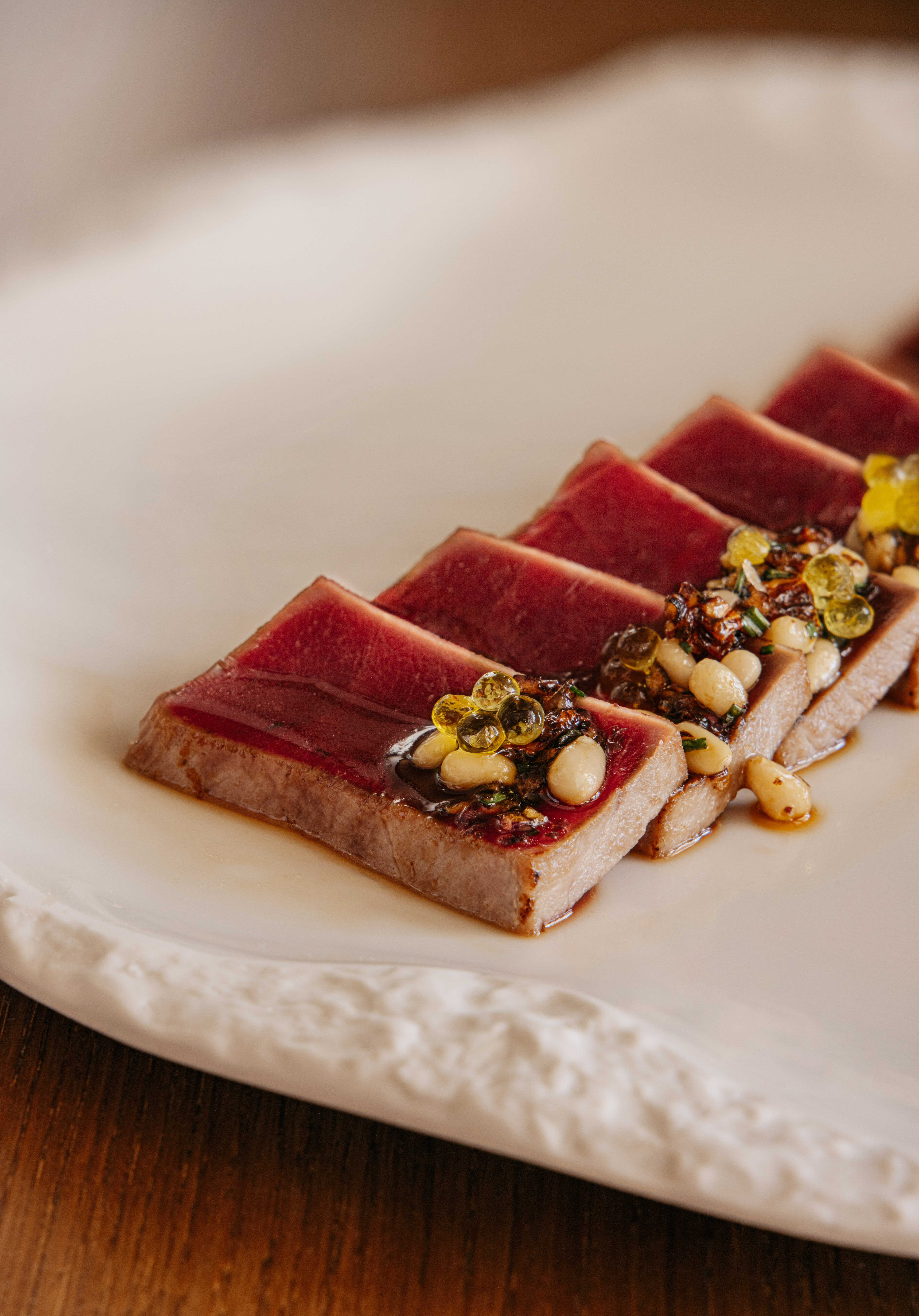 Seared tuna tataki with pine nuts, golden spheres, and savory sauce.