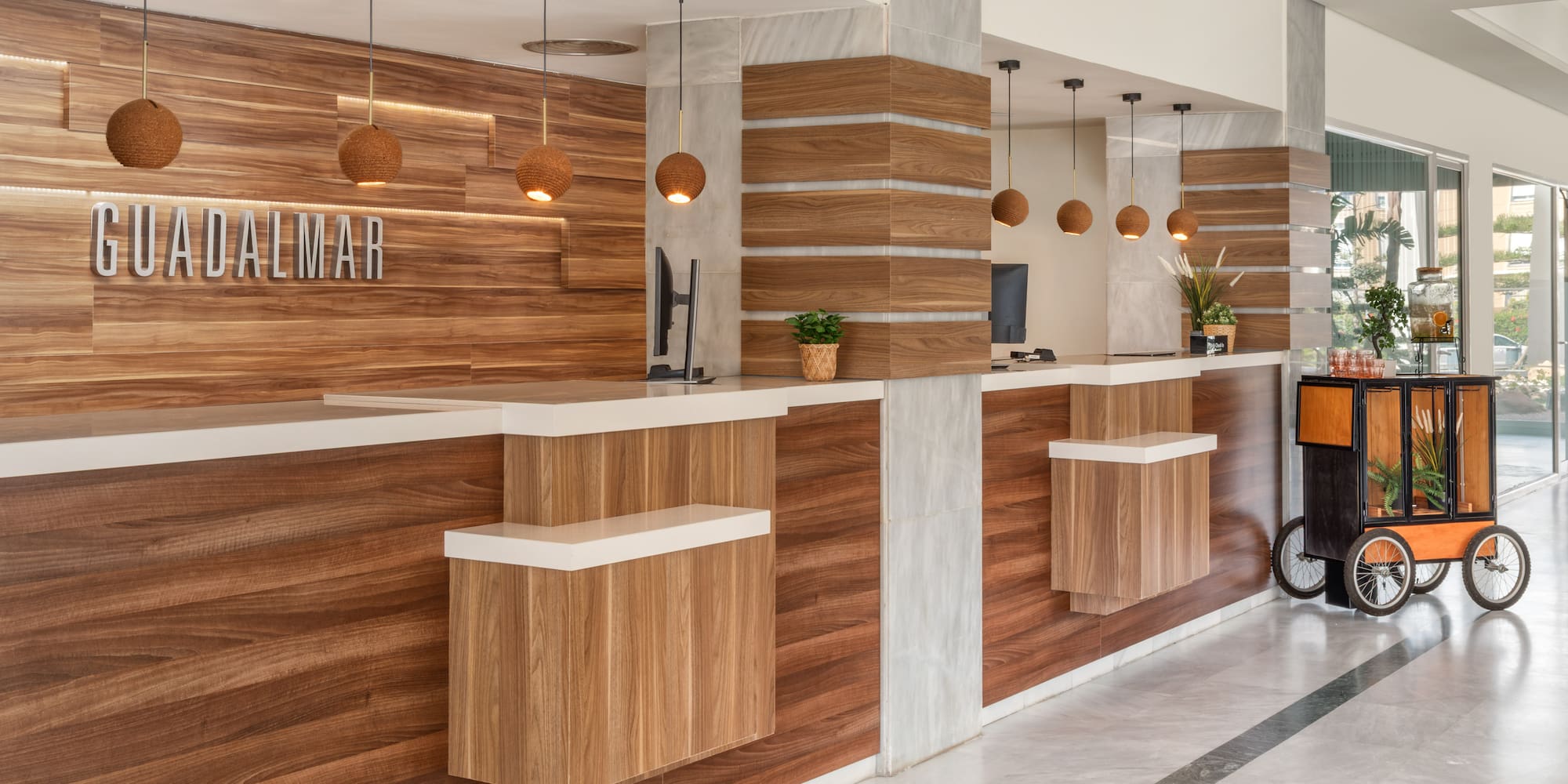 GUADALMAR hotel reception with modern wooden desks and pendant lights.