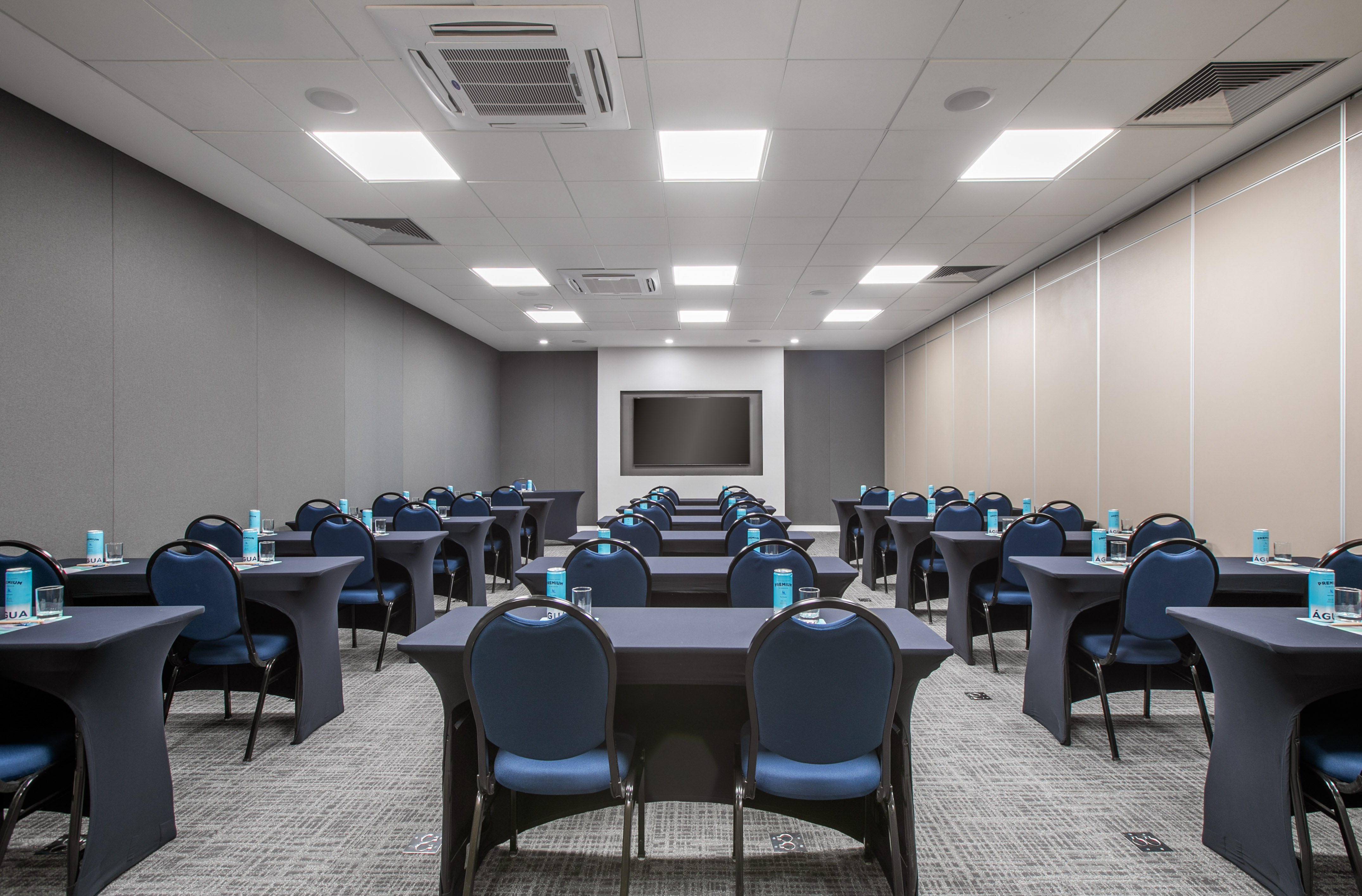 Conference room with blue chairs, black tables, large screen, ready for meetings.