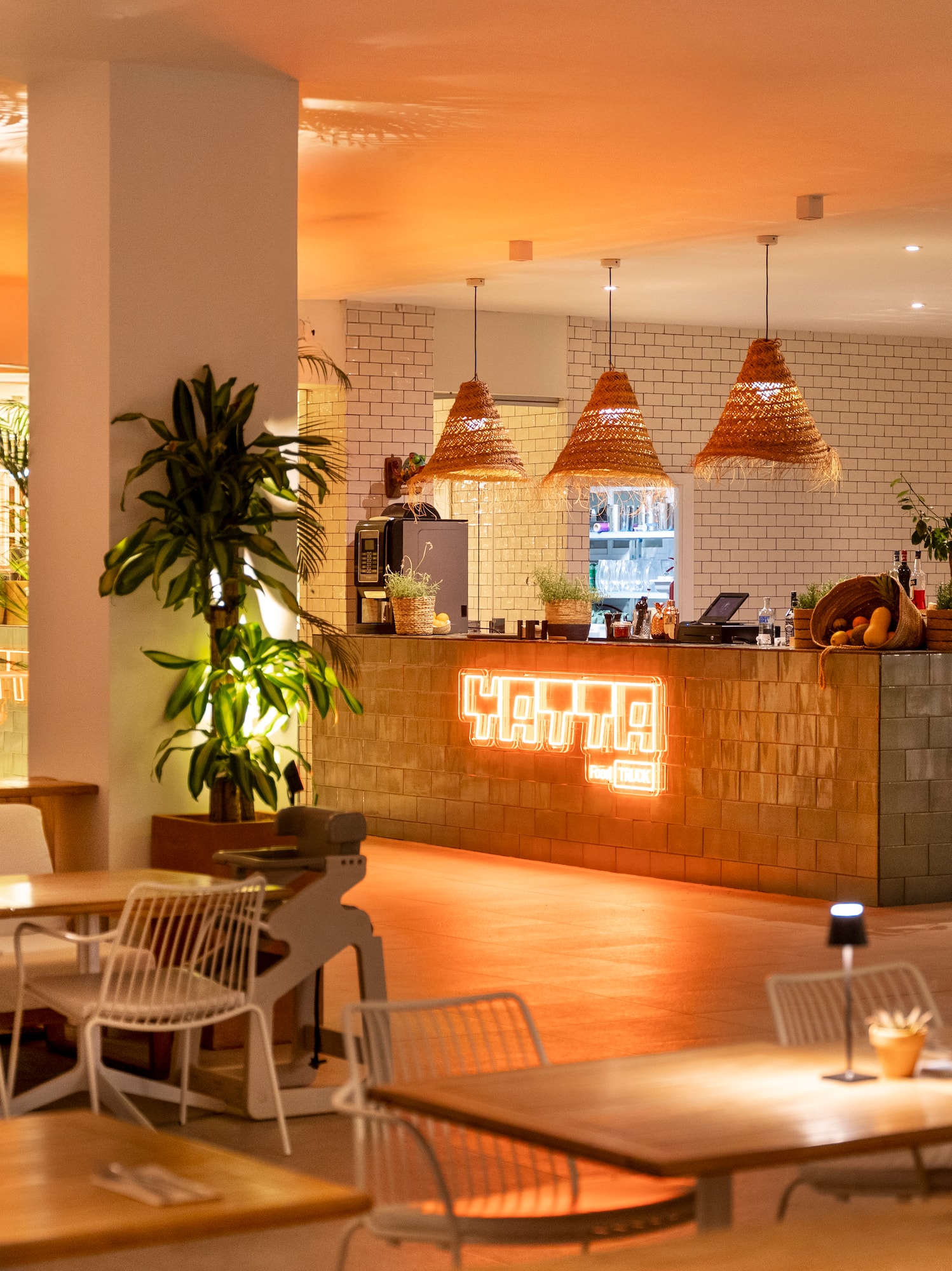 Modern restaurant bar with warm lighting, neon sign, and woven pendant lamps.