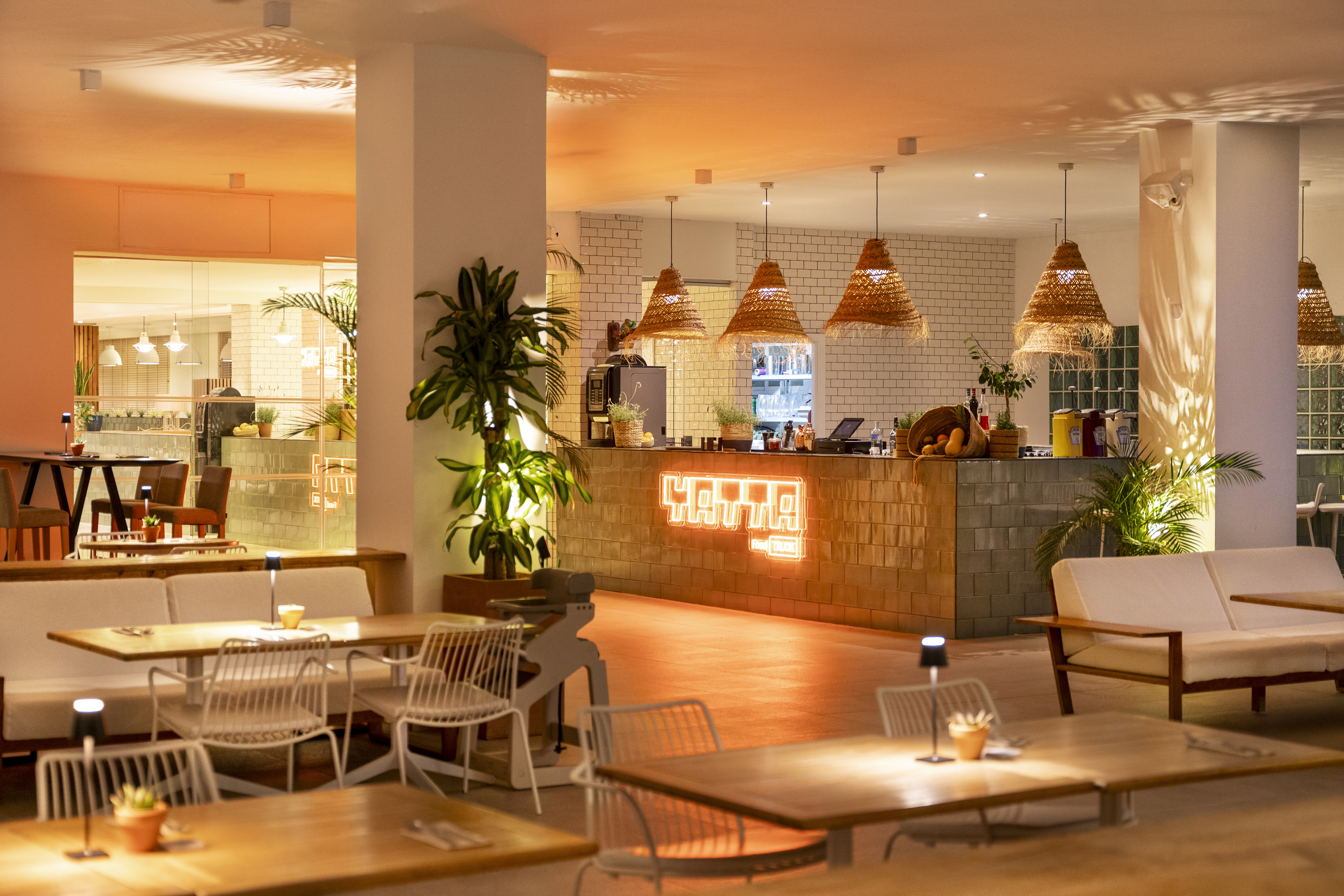 Modern restaurant bar with warm lighting, neon sign, and woven pendant lamps.