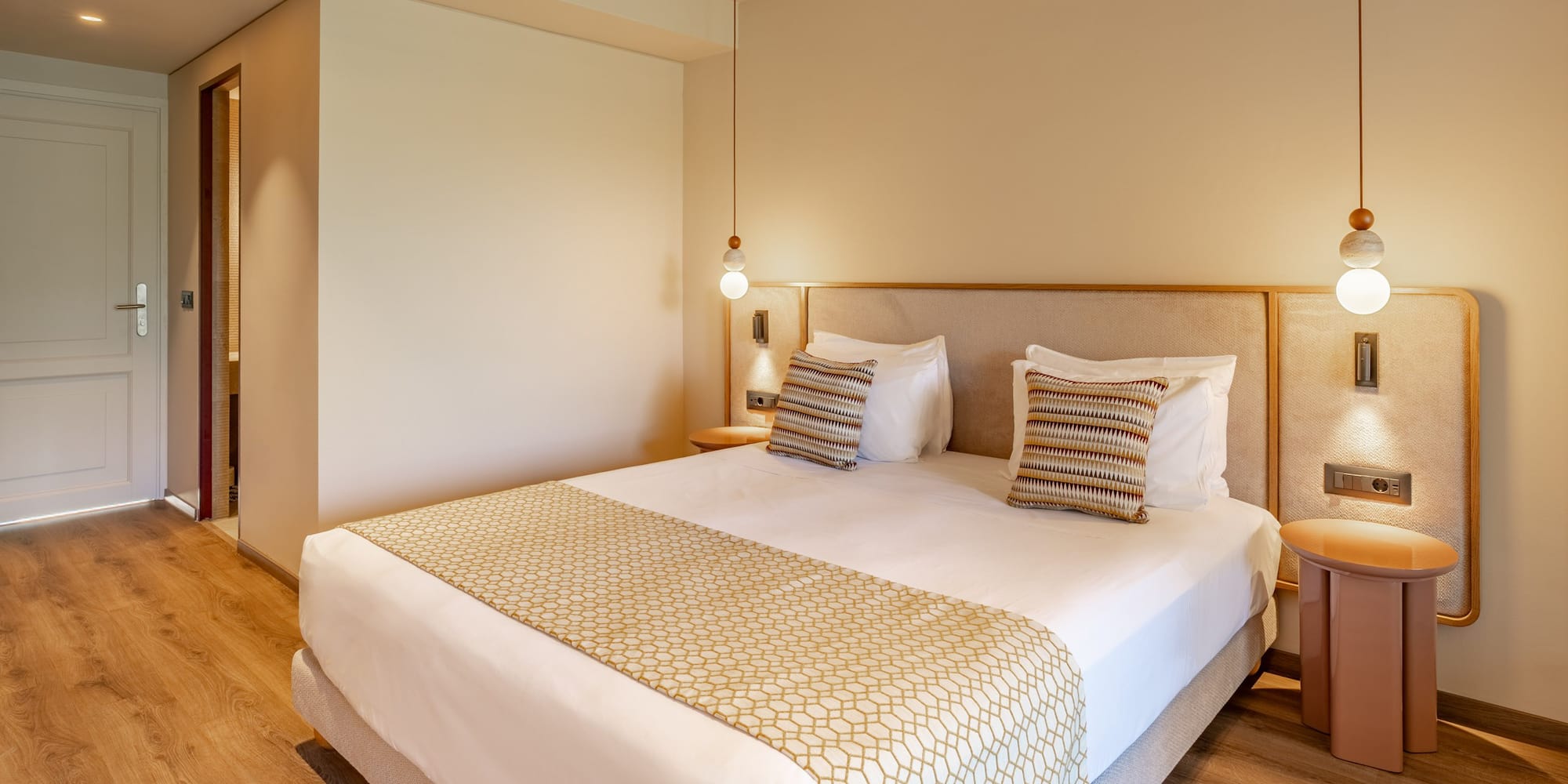 Modern hotel room with king bed, patterned runner, and warm pendant lighting.