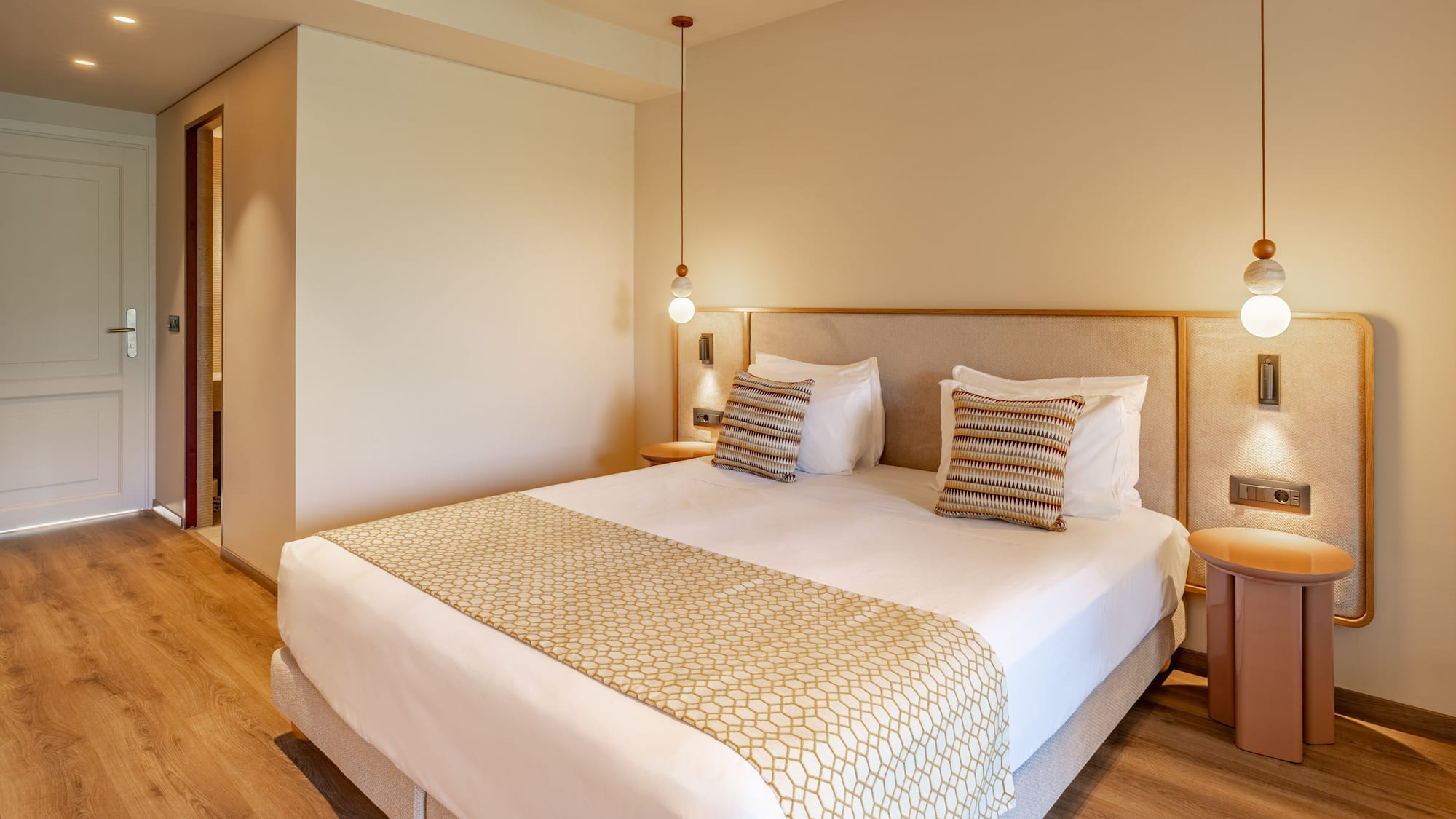 Modern hotel room with king bed, patterned runner, and warm pendant lighting.