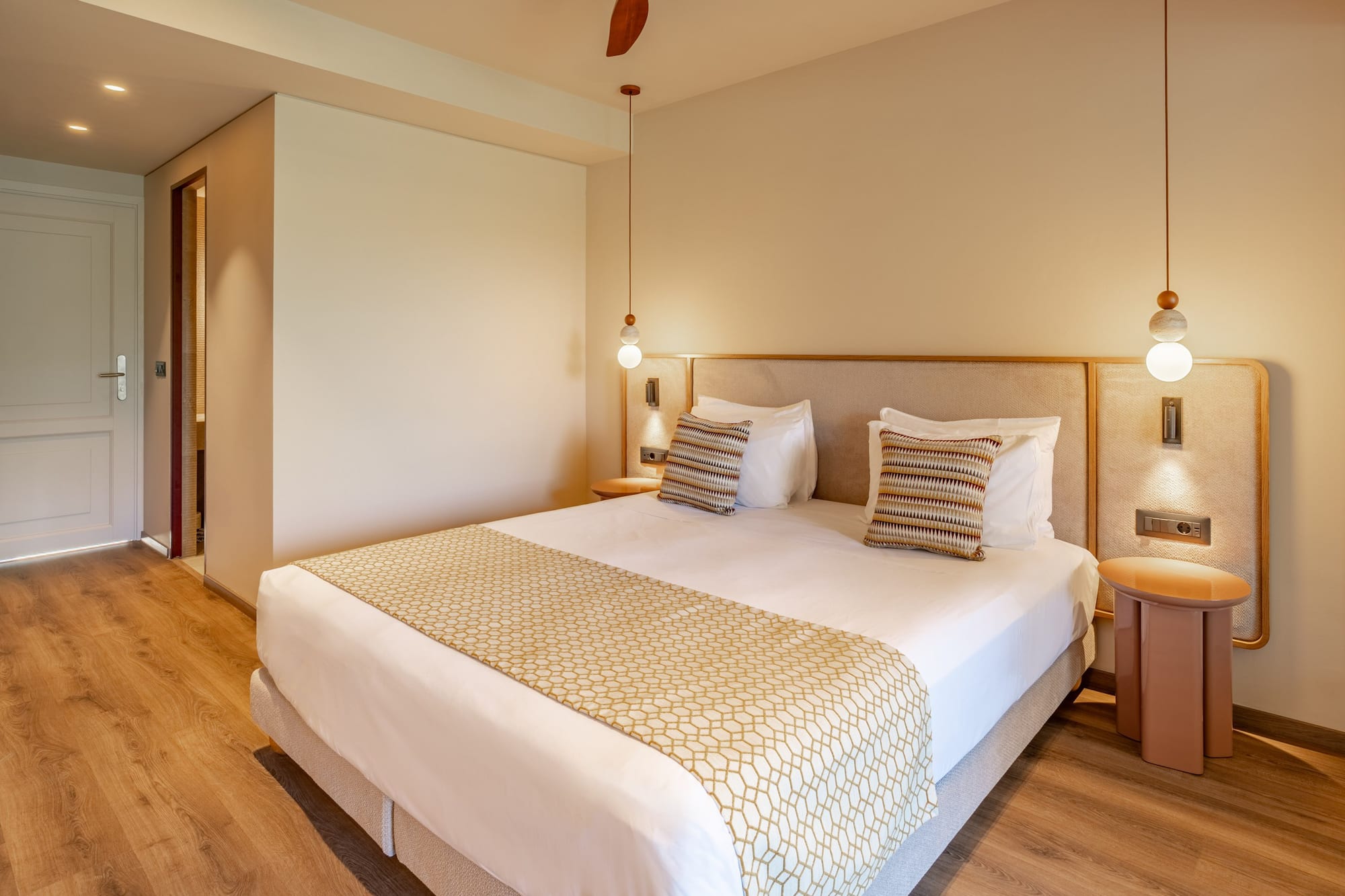 Modern hotel room with king bed, patterned runner, and warm pendant lighting.
