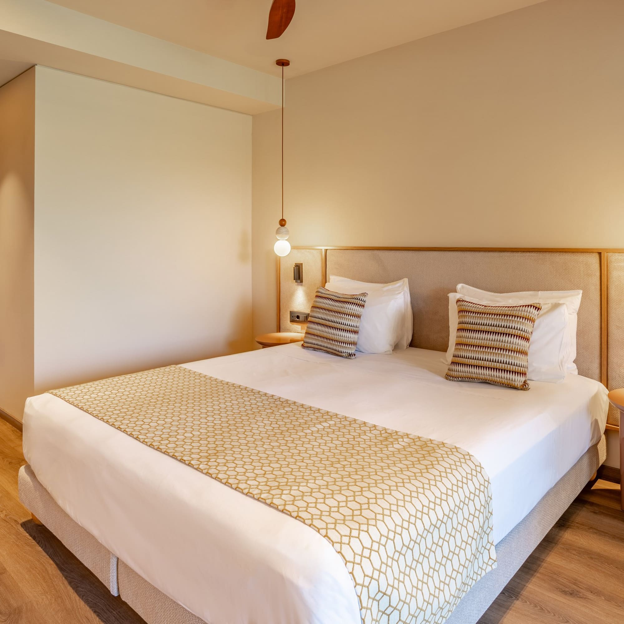Modern hotel room with king bed, patterned runner, and warm pendant lighting.