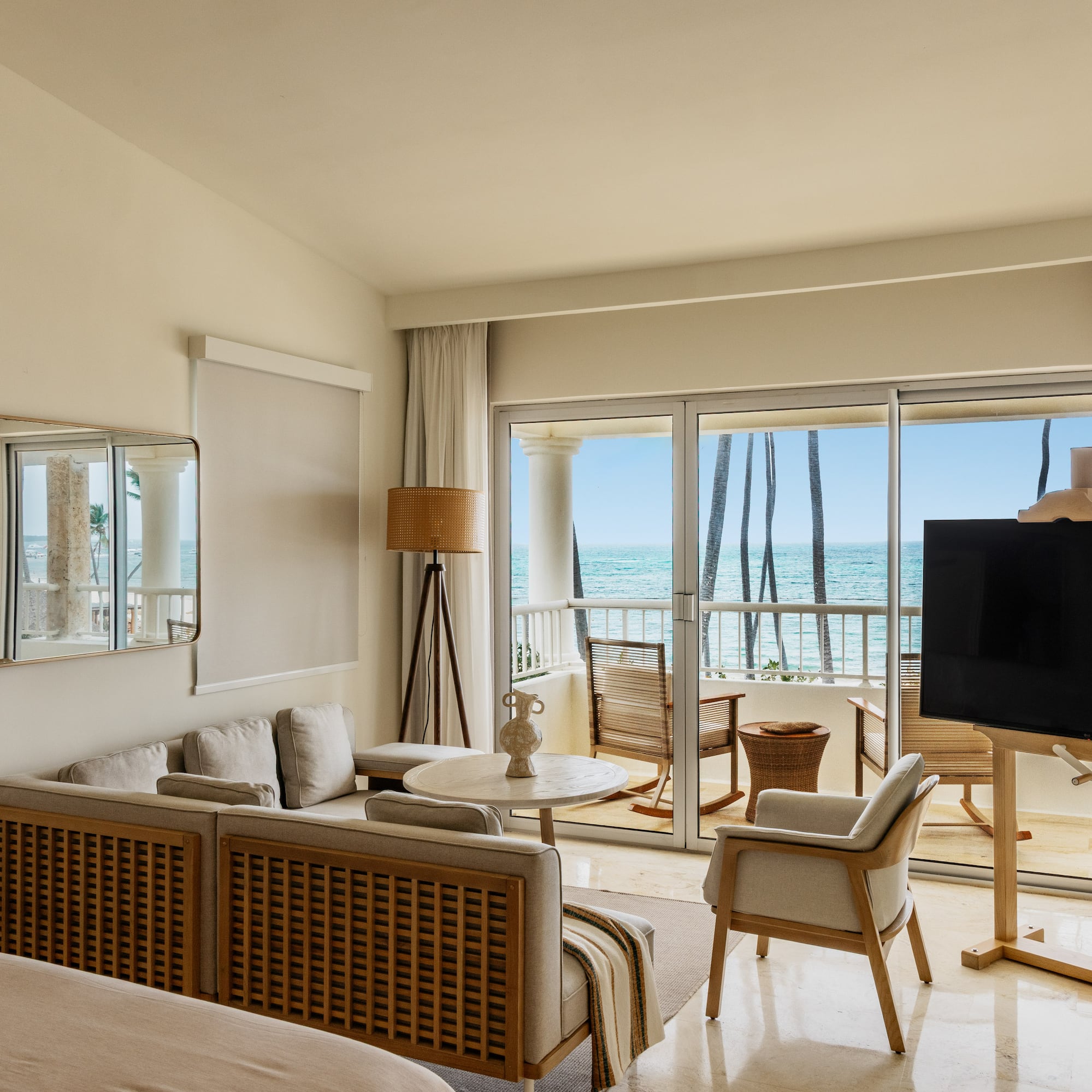 Luxury hotel suite overlooking ocean, modern decor, balcony, and palm trees.