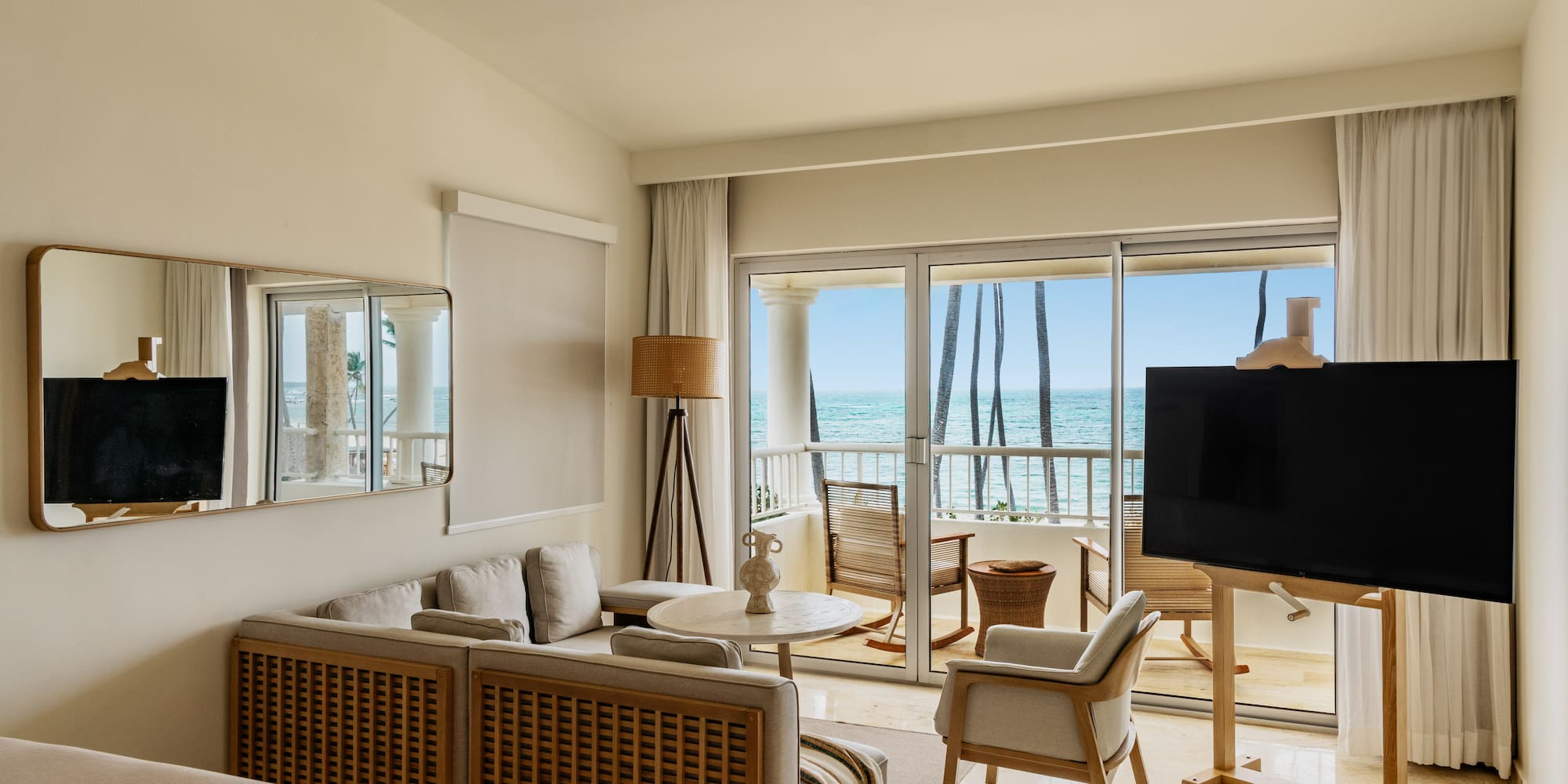 Luxury hotel suite overlooking ocean, modern decor, balcony, and palm trees.