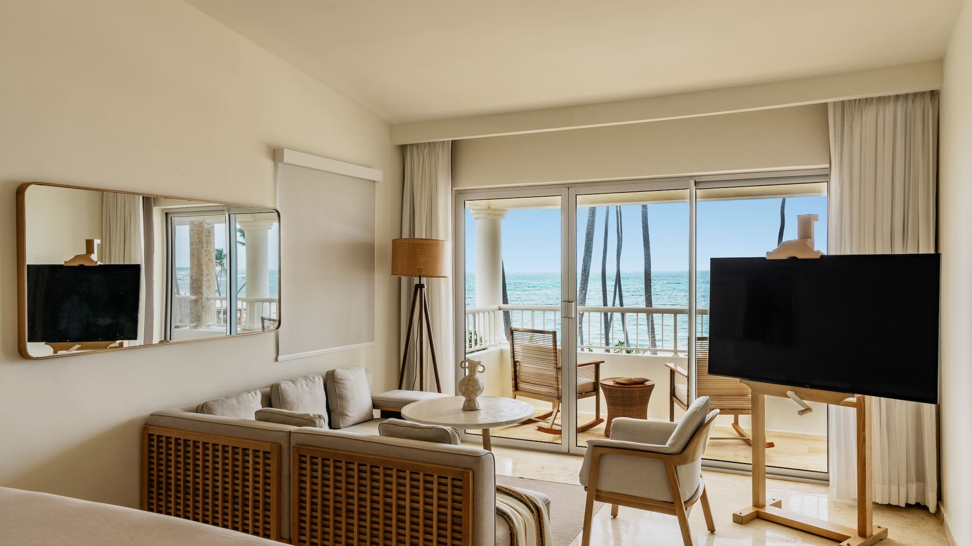 Luxury hotel suite overlooking ocean, modern decor, balcony, and palm trees.