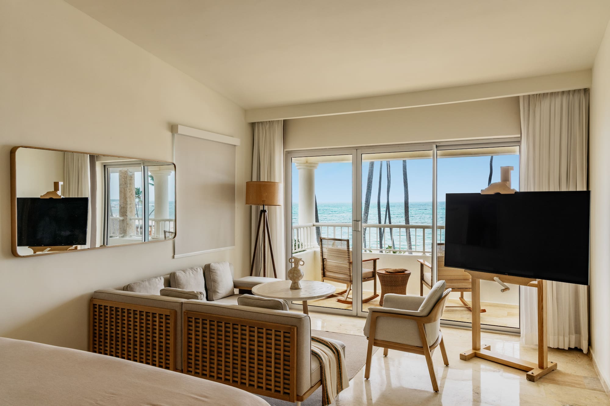 Luxury hotel suite overlooking ocean, modern decor, balcony, and palm trees.