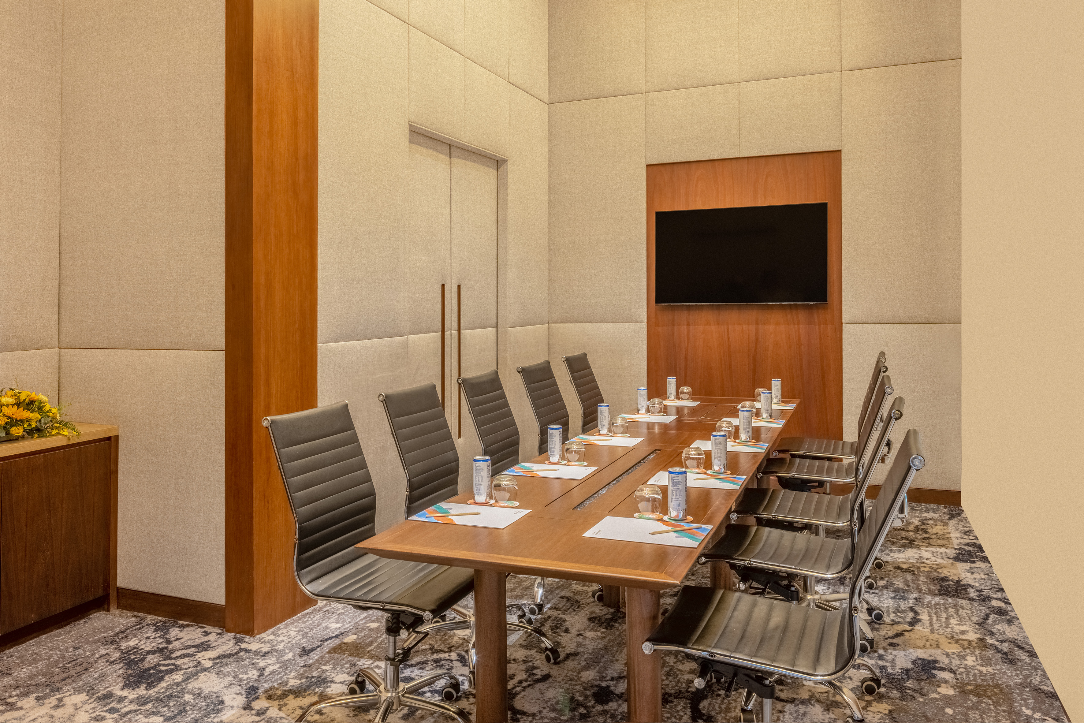 Modern meeting room with wooden conference table, black chairs, and large TV screen.