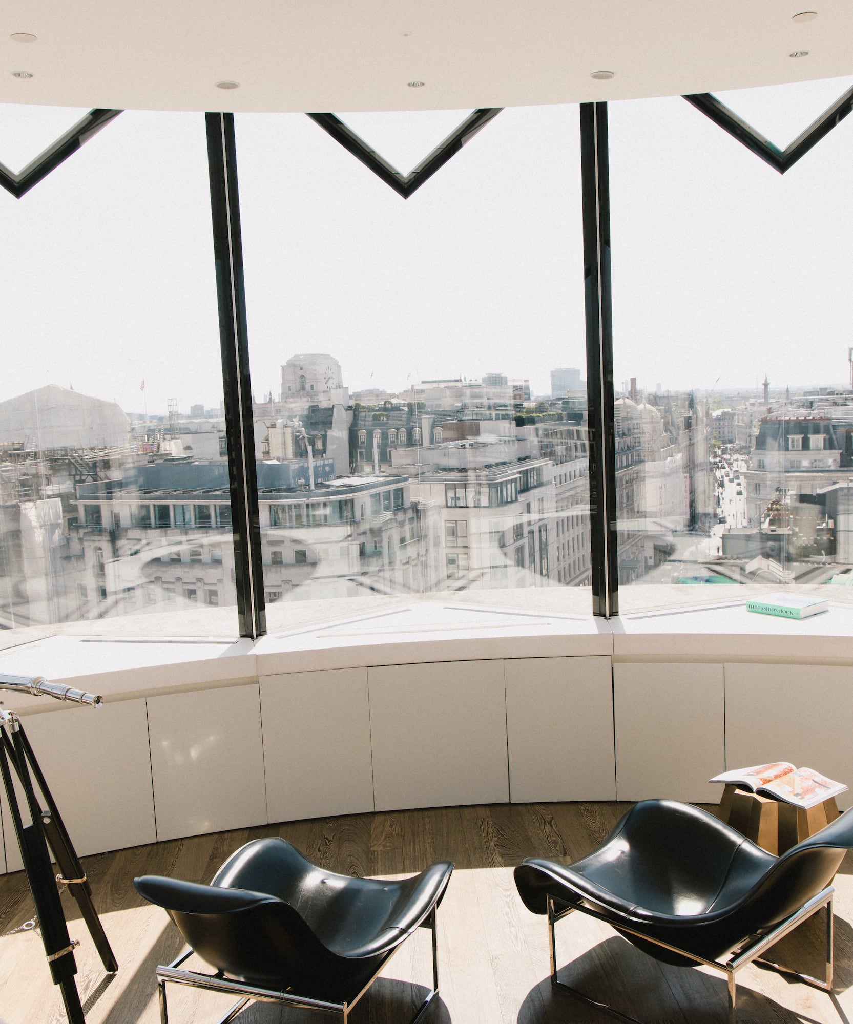 Panoramic London city view from modern lounge with telescope and black chairs.