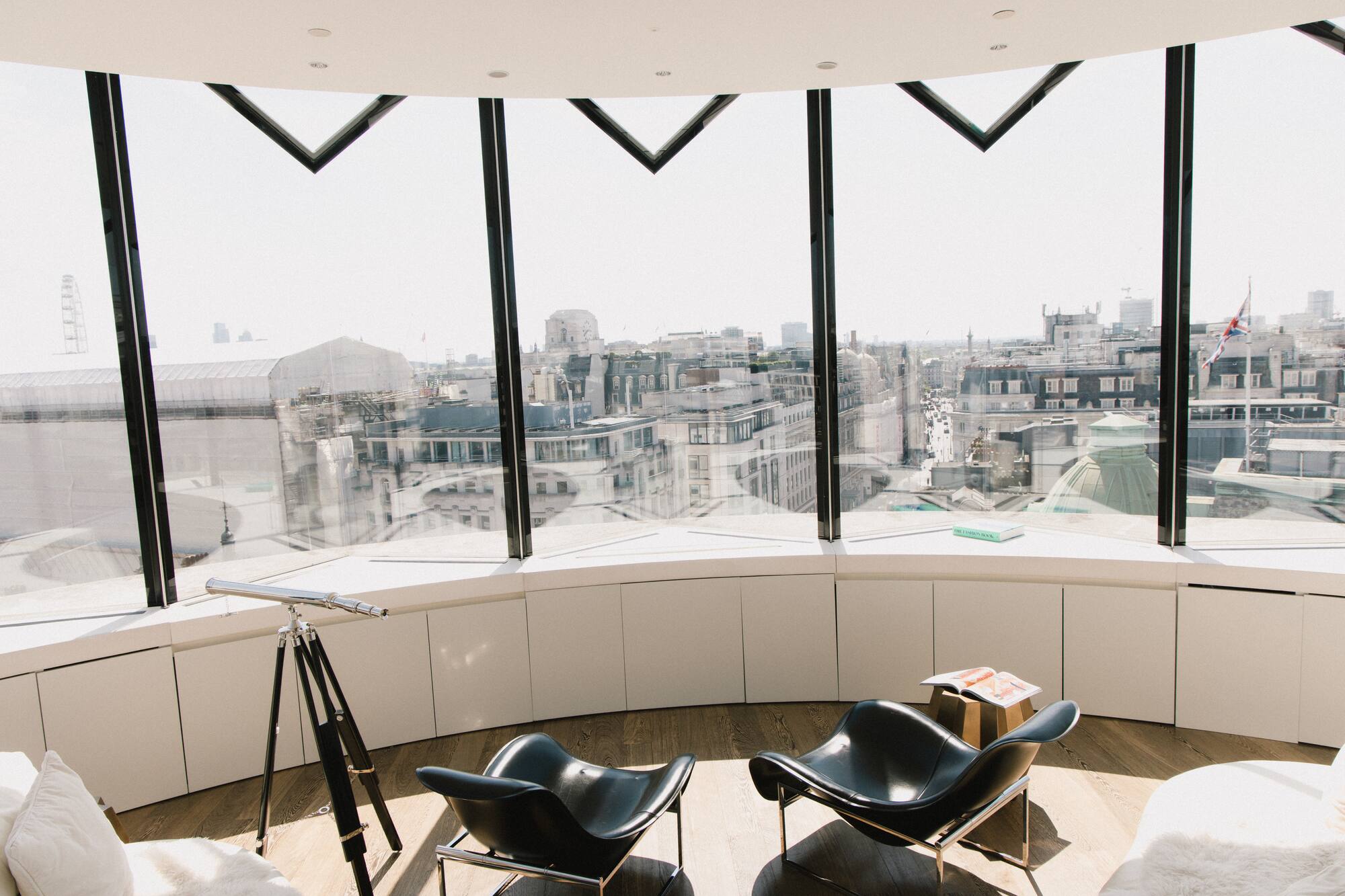 Panoramic London city view from modern lounge with telescope and black chairs.