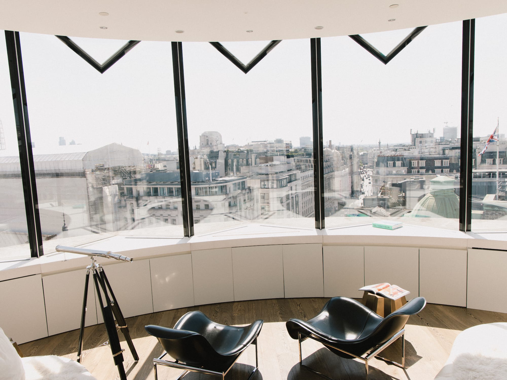 Panoramic London city view from modern lounge with telescope and black chairs.