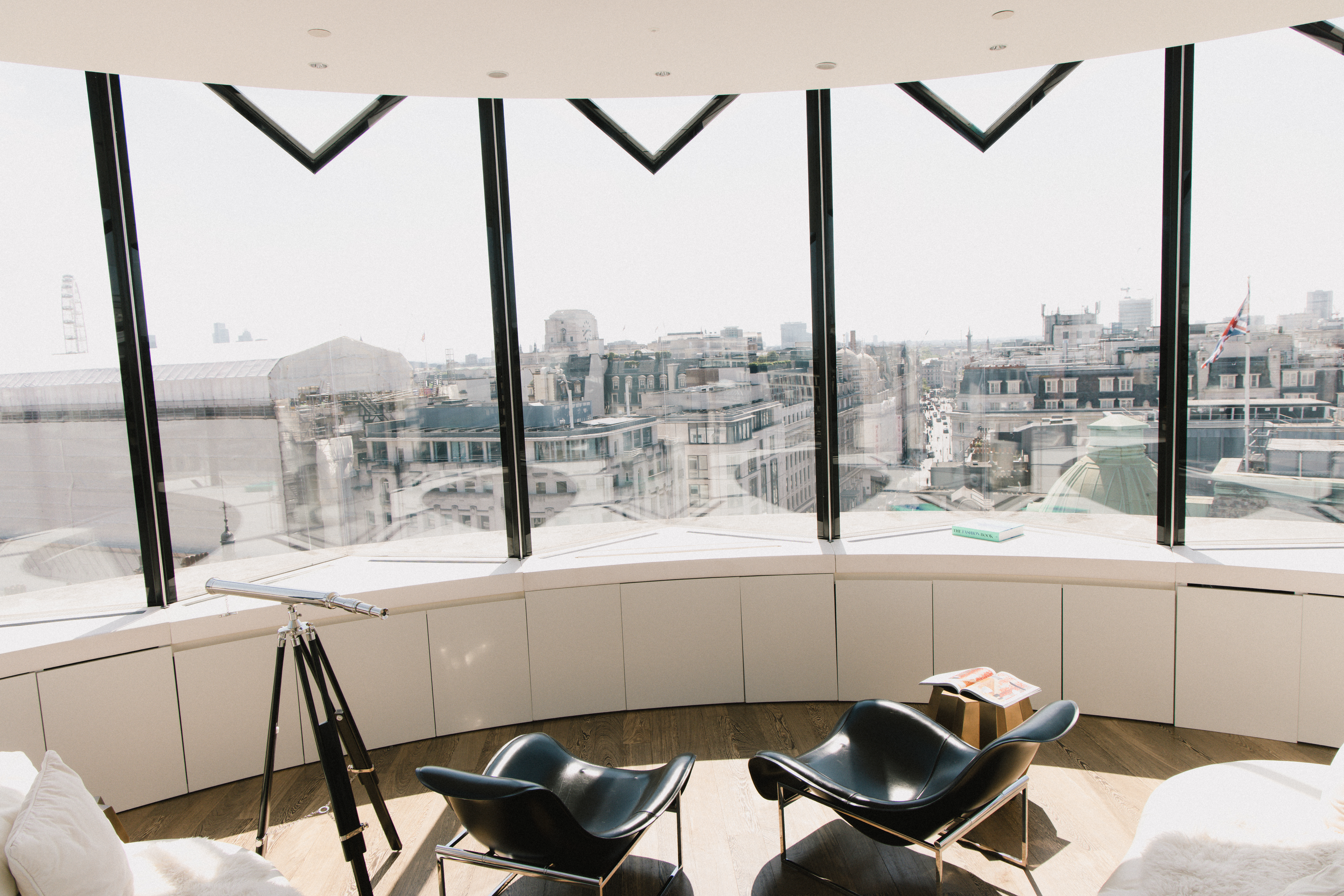 Panoramic London city view from modern lounge with telescope and black chairs.