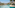 Tropical resort pool with modern buildings, palm trees, and sun loungers.