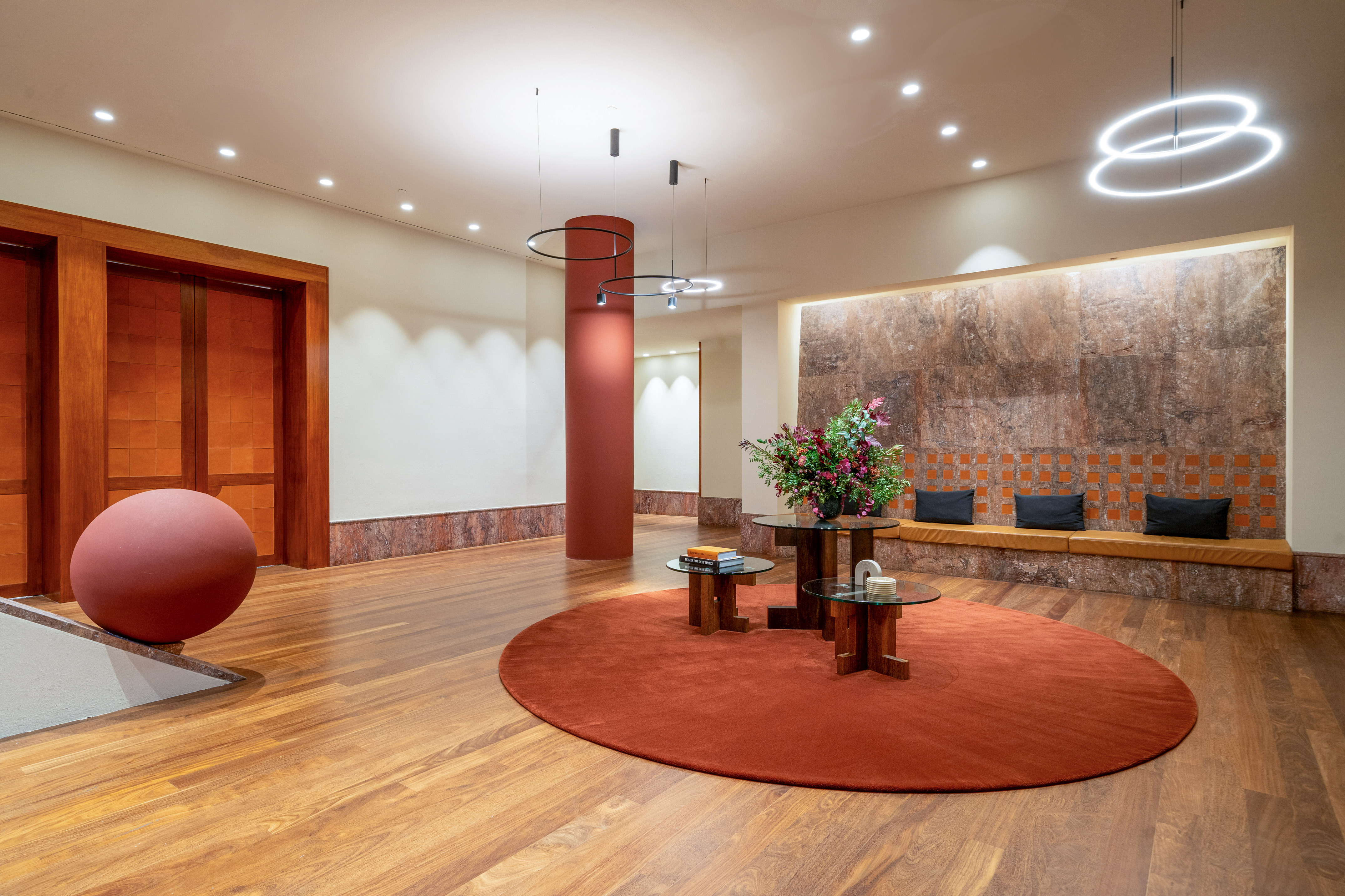 Modern hotel lobby with red rug, wood floors, and architectural stone wall.