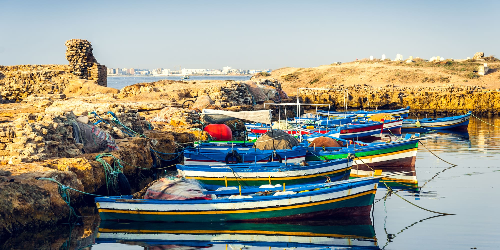 Barcos de pesca coloridos amarrados en costa rocosa bajo cielo azul.