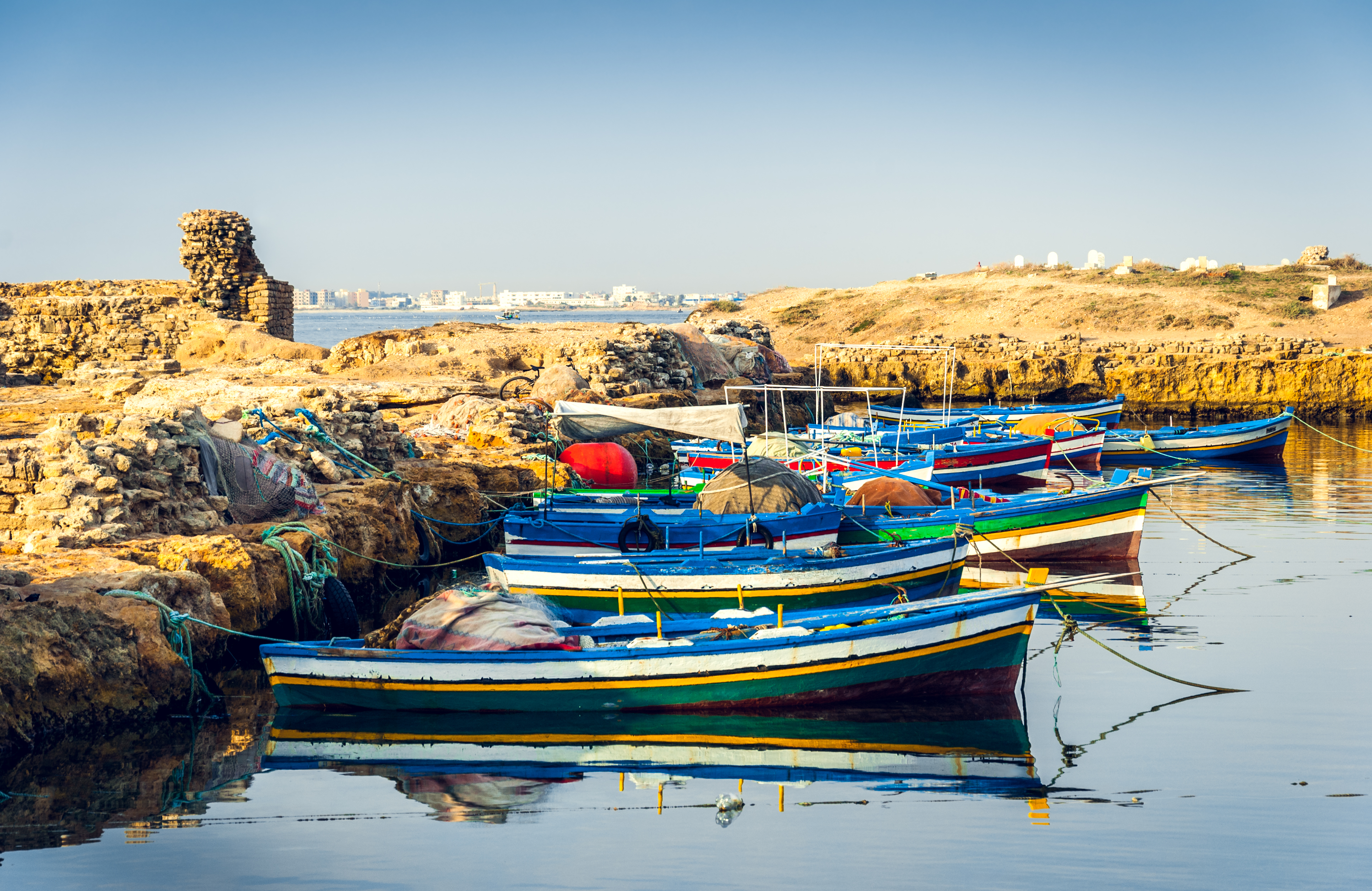 Barcos de pesca coloridos amarrados en costa rocosa bajo cielo azul.