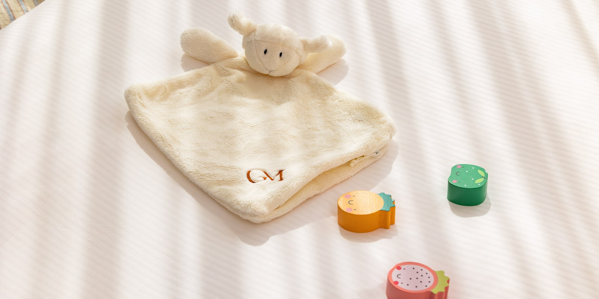 Lamb baby lovey (GM monogrammed) with wooden fruit toys on white bedding.