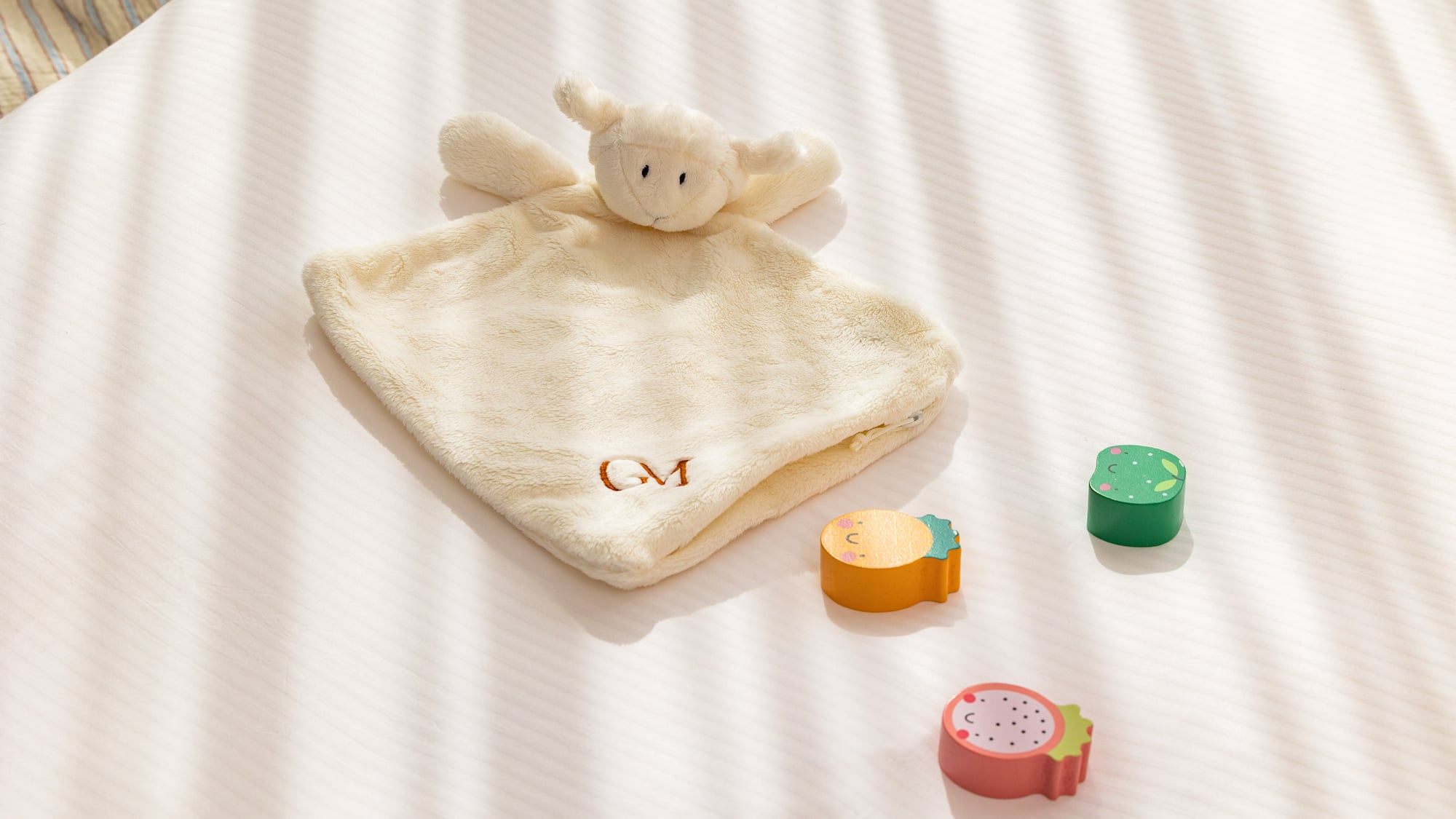 Lamb baby lovey (GM monogrammed) with wooden fruit toys on white bedding.
