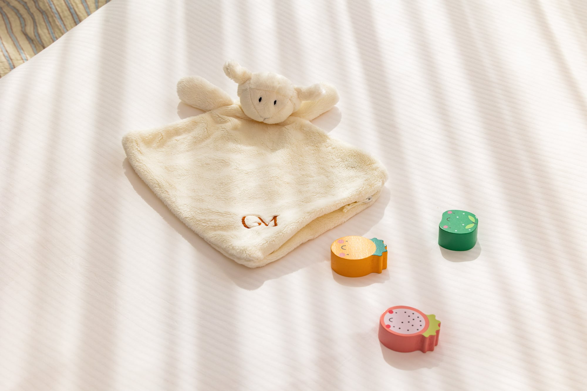 Lamb baby lovey (GM monogrammed) with wooden fruit toys on white bedding.