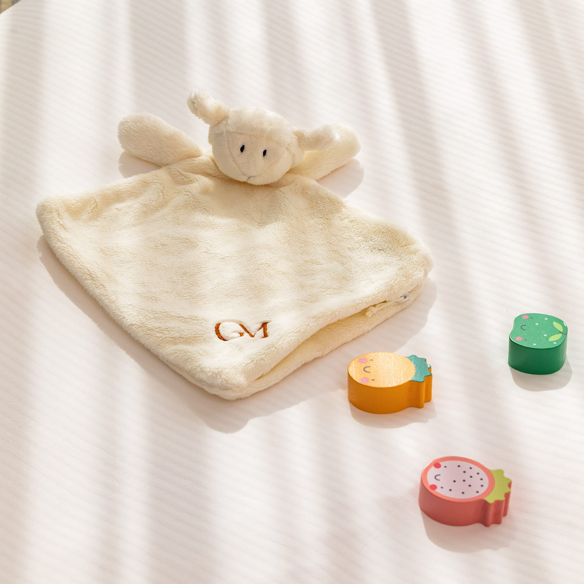 Lamb baby lovey (GM monogrammed) with wooden fruit toys on white bedding.