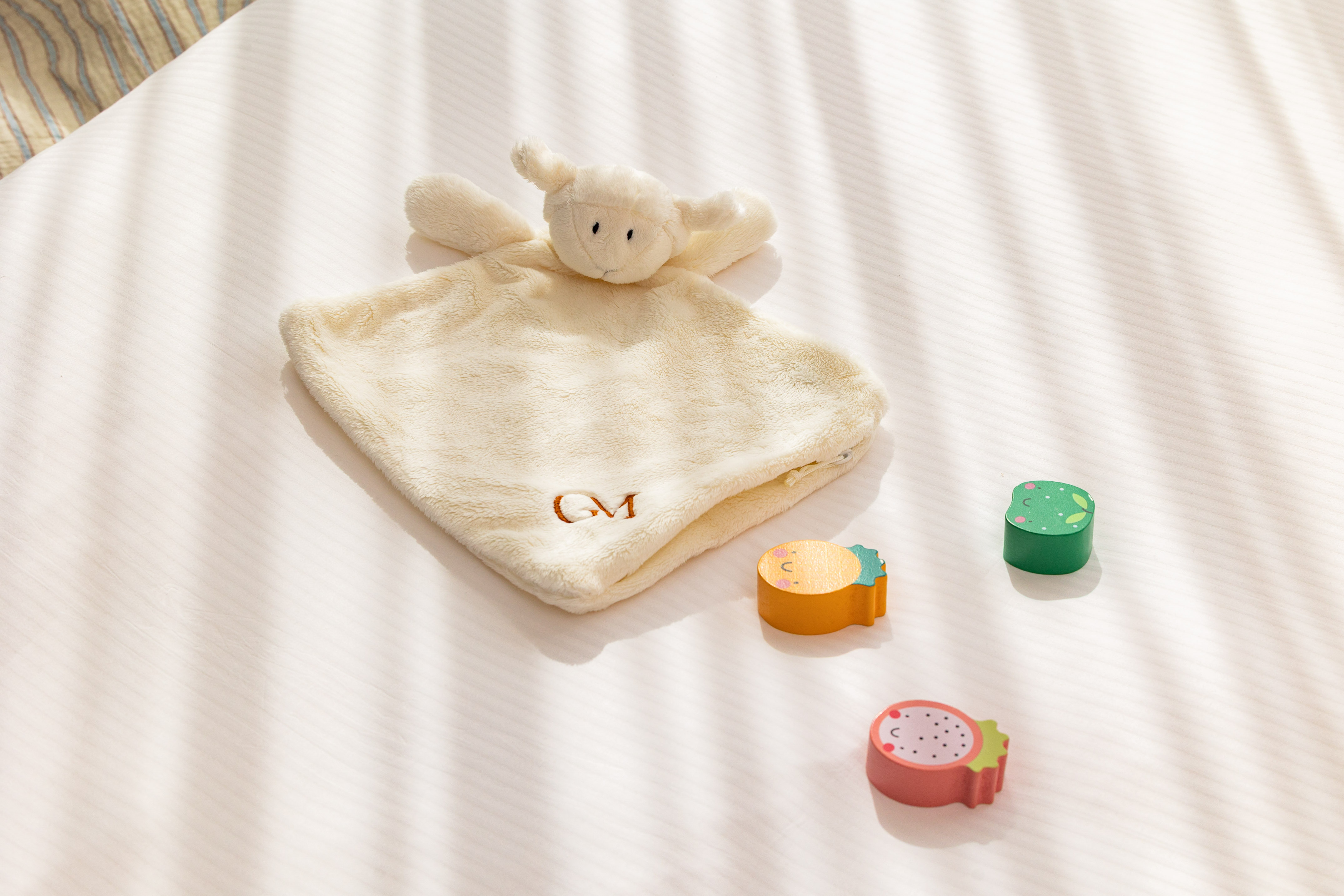 Lamb baby lovey (GM monogrammed) with wooden fruit toys on white bedding.