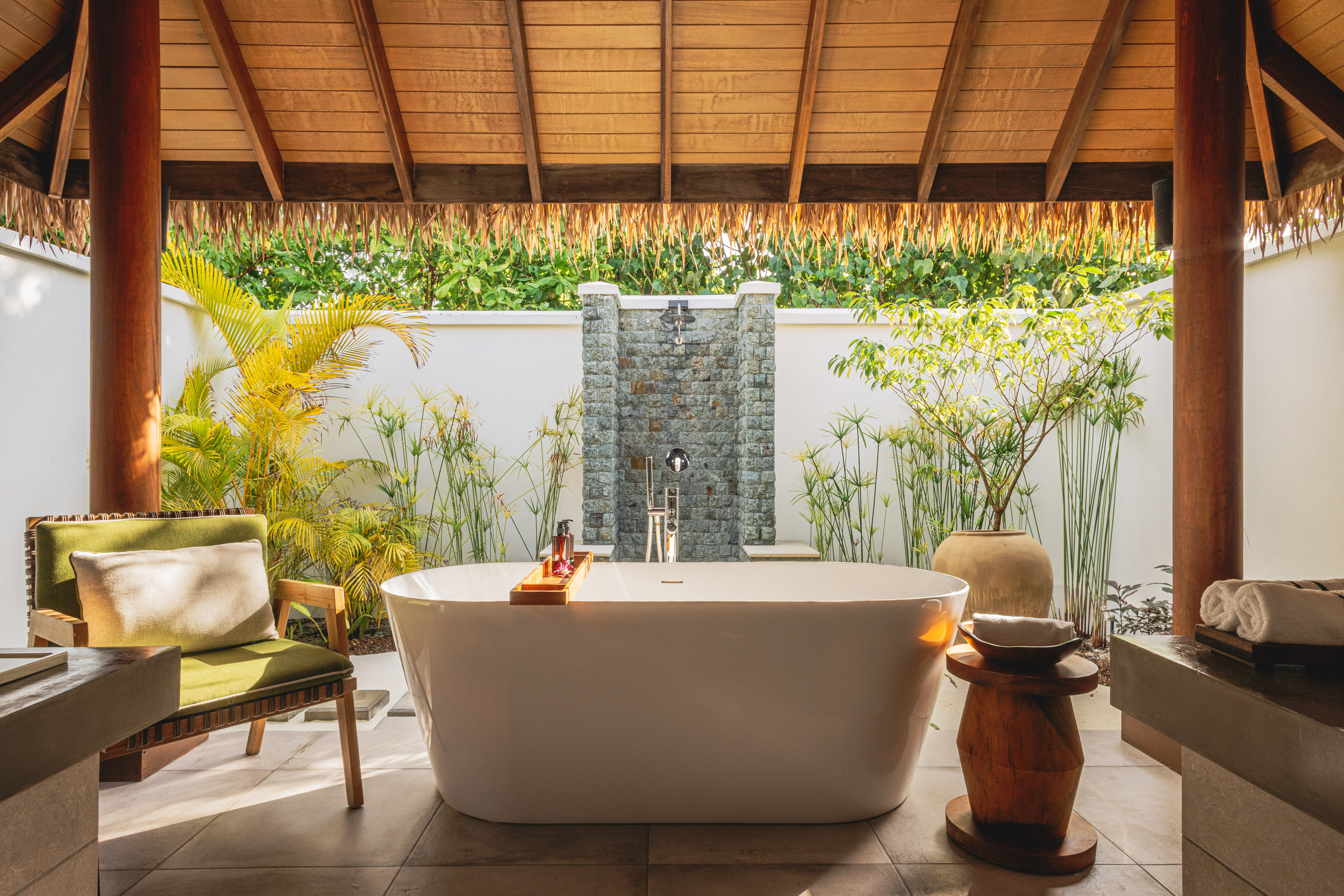 Luxury outdoor bathroom with freestanding tub, stone shower, tropical plants.