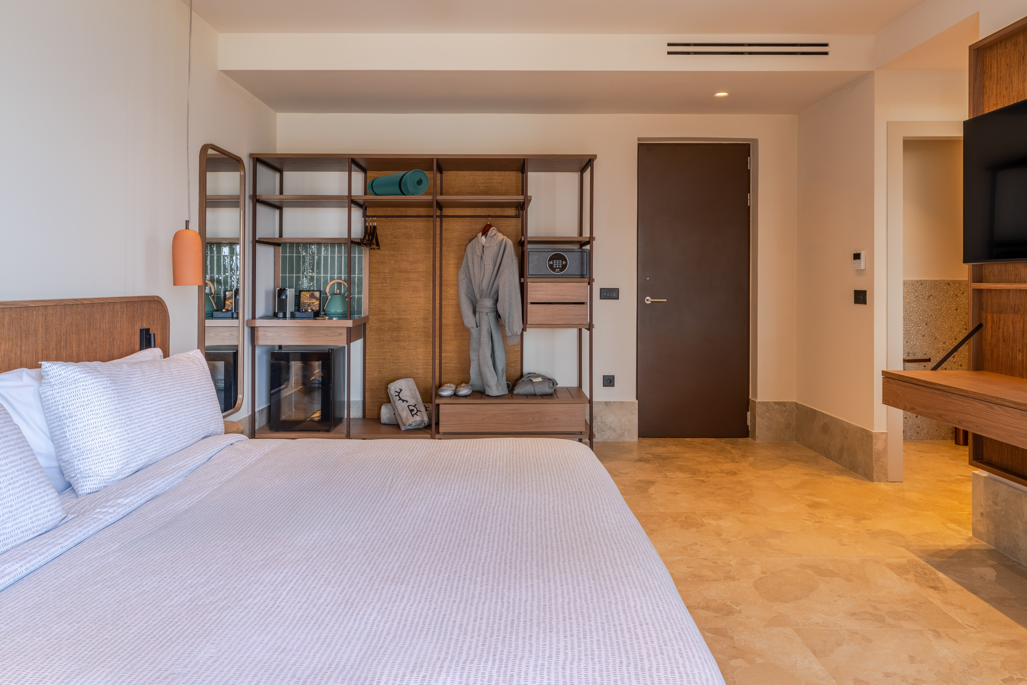 Stylish hotel room: King bed, wooden wardrobe, robe, safe, and mini-bar setup.