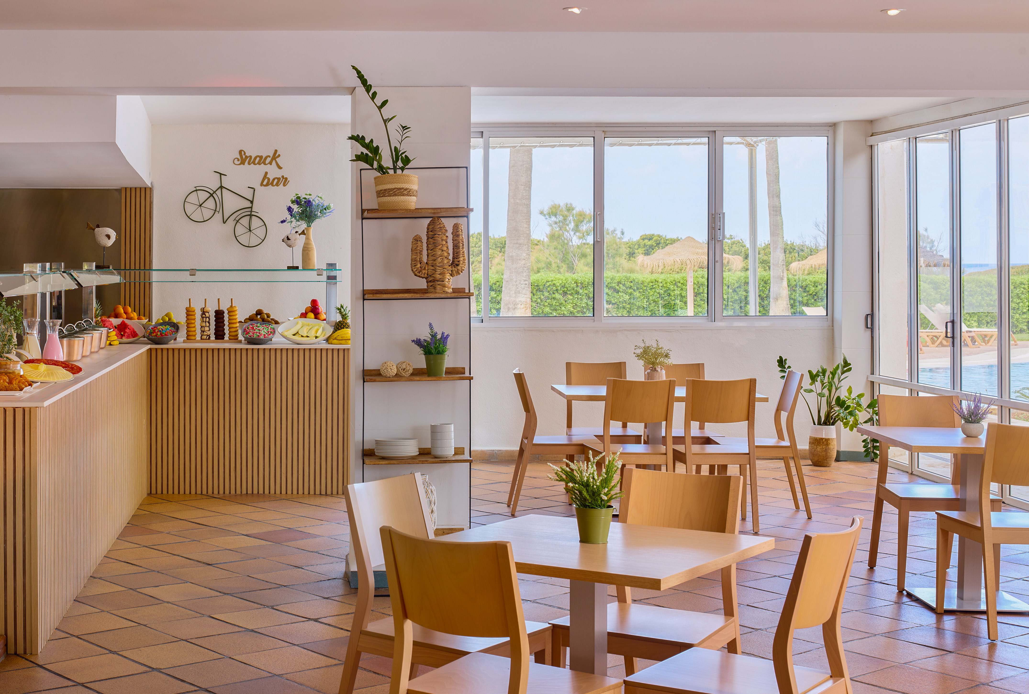 Snack bar buffet with fresh fruit, dining tables, and outdoor pool view.