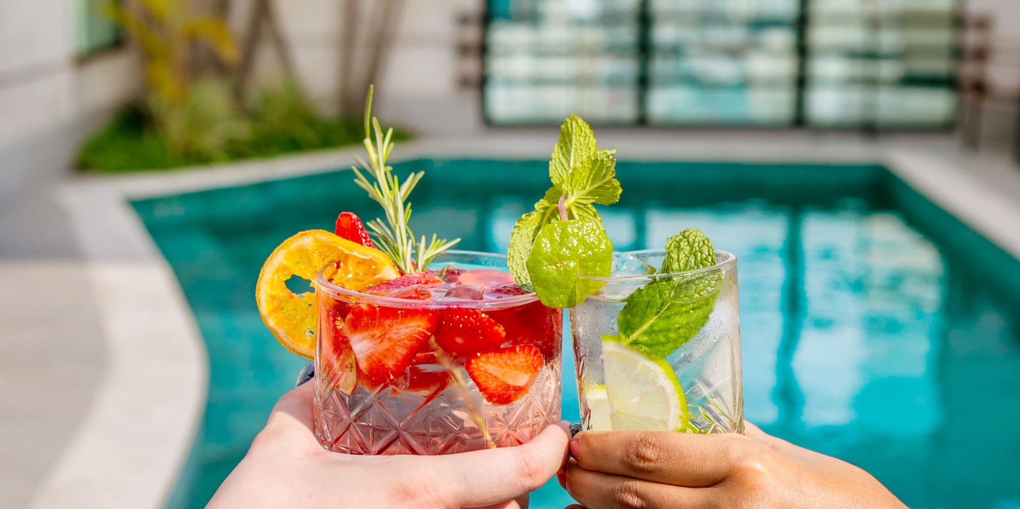 a pair of hands holding drinks next to a pool