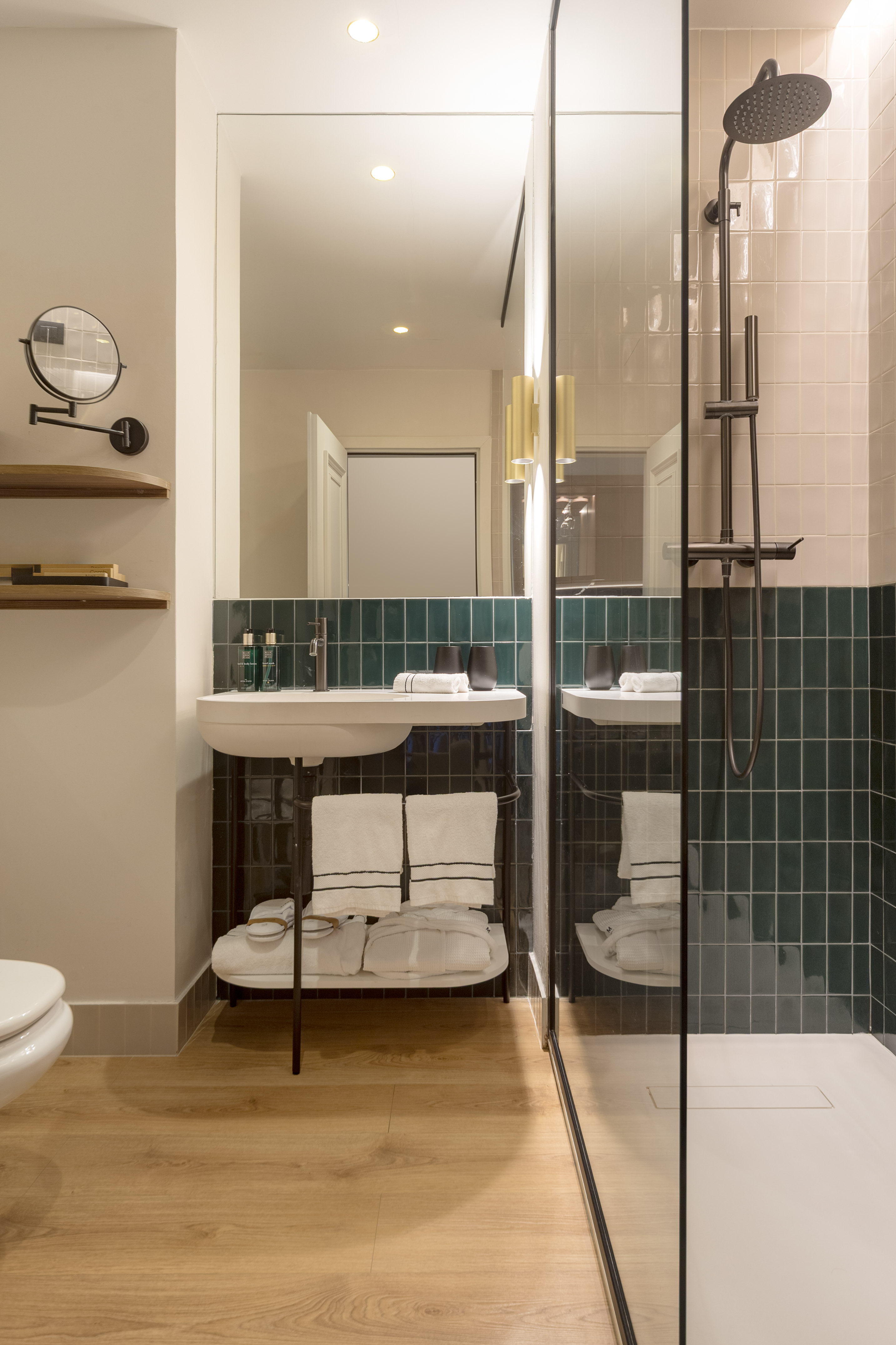 Modern hotel bathroom with teal subway tiles, white sink, and glass shower.